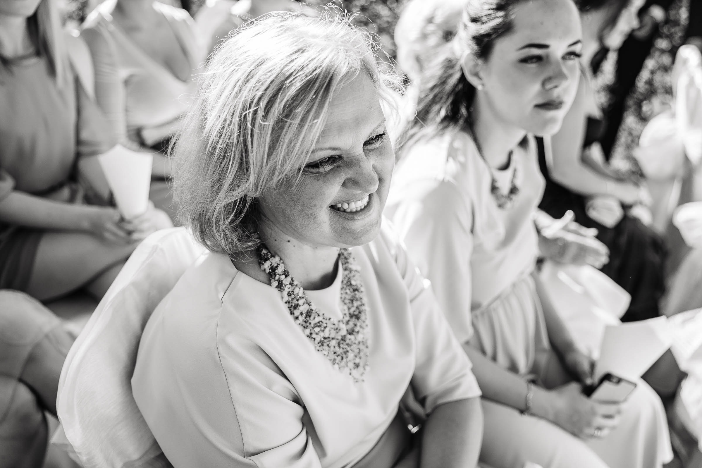 Guests smiling during ceremony in garden, by Tanya Bogdan, Exeter reportage wedding photographer.  