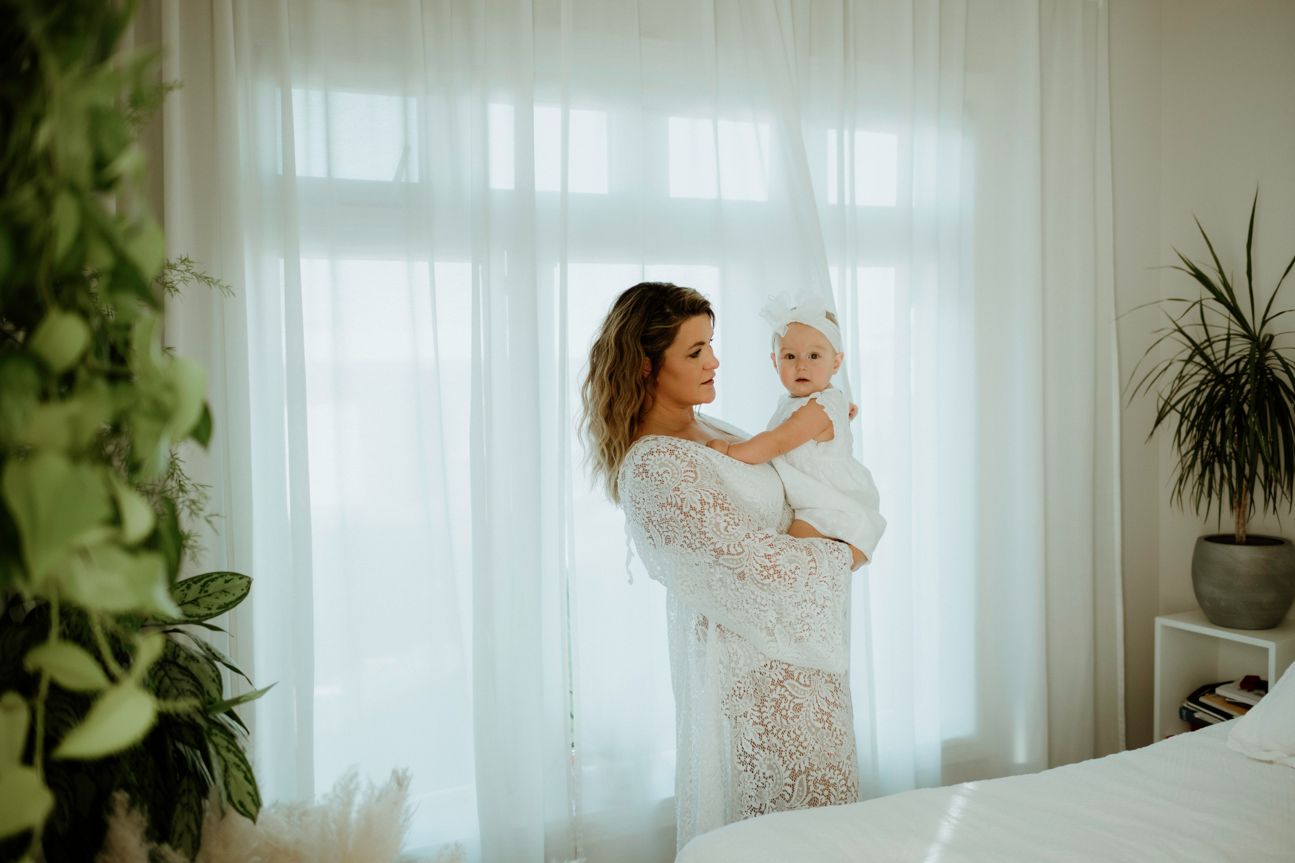 An enchanting outdoor maternity photoshoot at the client's house. The image features a radiant mother and her daughter, both elegantly dressed in white, against the backdrop of their home. The simplicity of their attire and the natural surroundings creates a timeless and intimate atmosphere. Book a personalized outdoor session with MD Studio to capture beautiful moments in the comfort of your own home