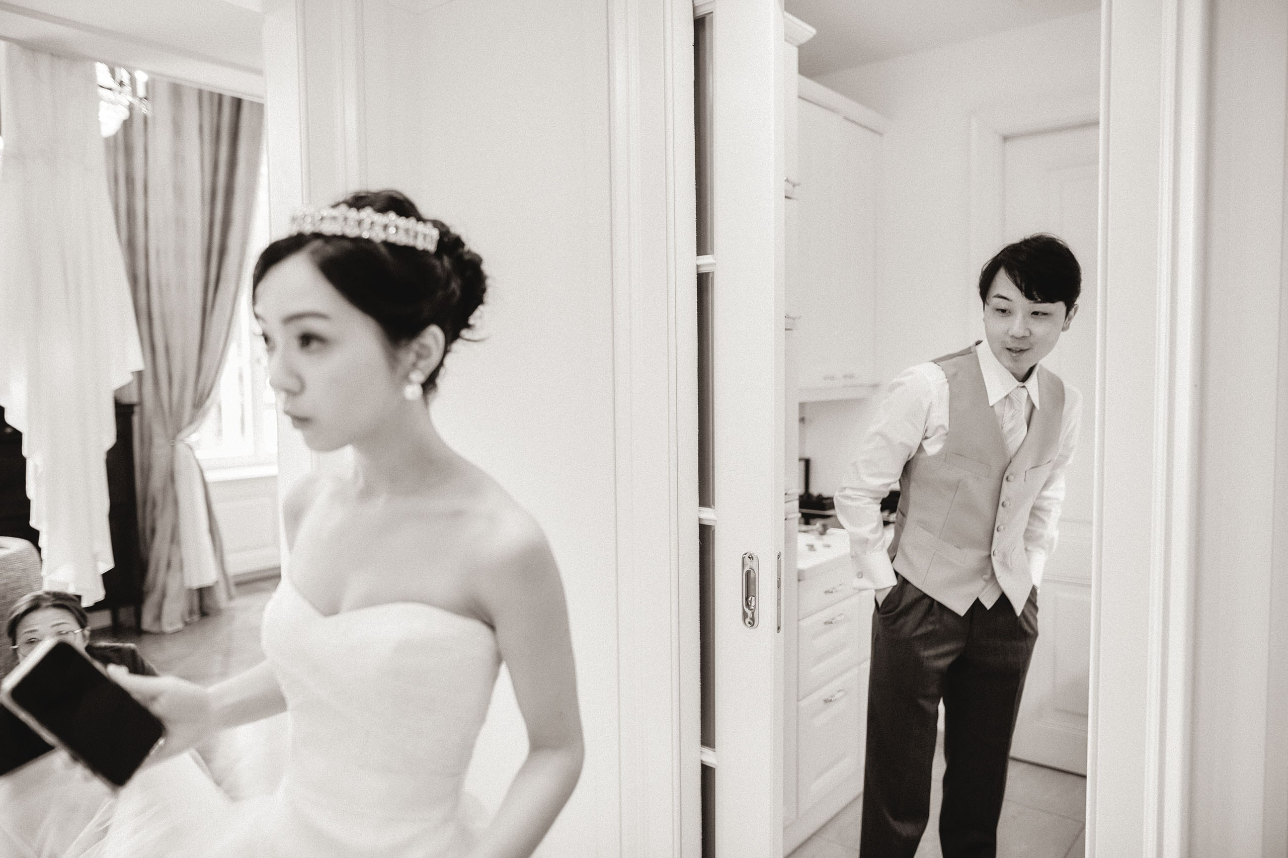 The groom checks on his bride as she views herself in the mirror of their suite.