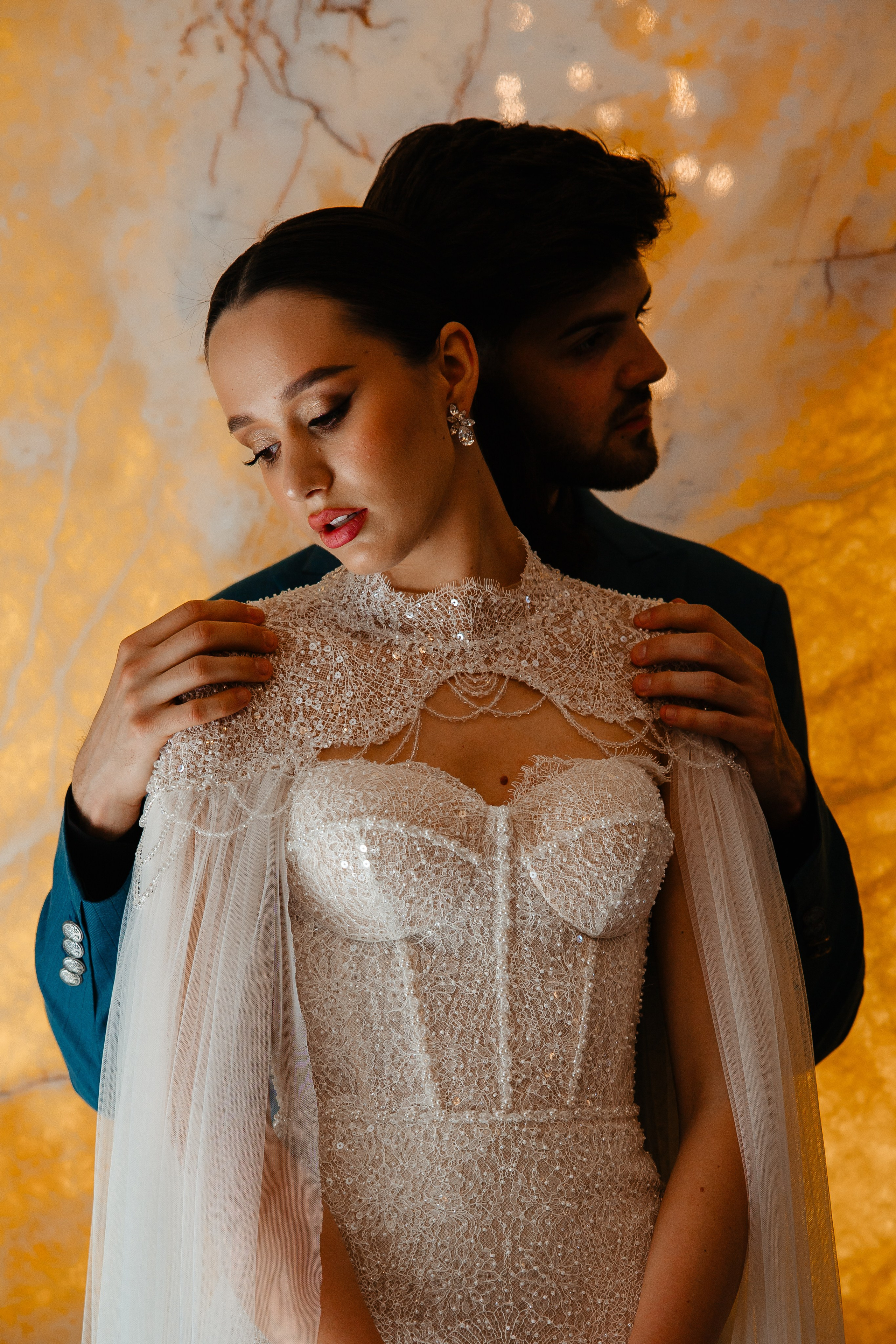 Cuplu îmbrățișat romantic, mireasa purtând o rochie decorată cu cristale, fundal cald marmorat