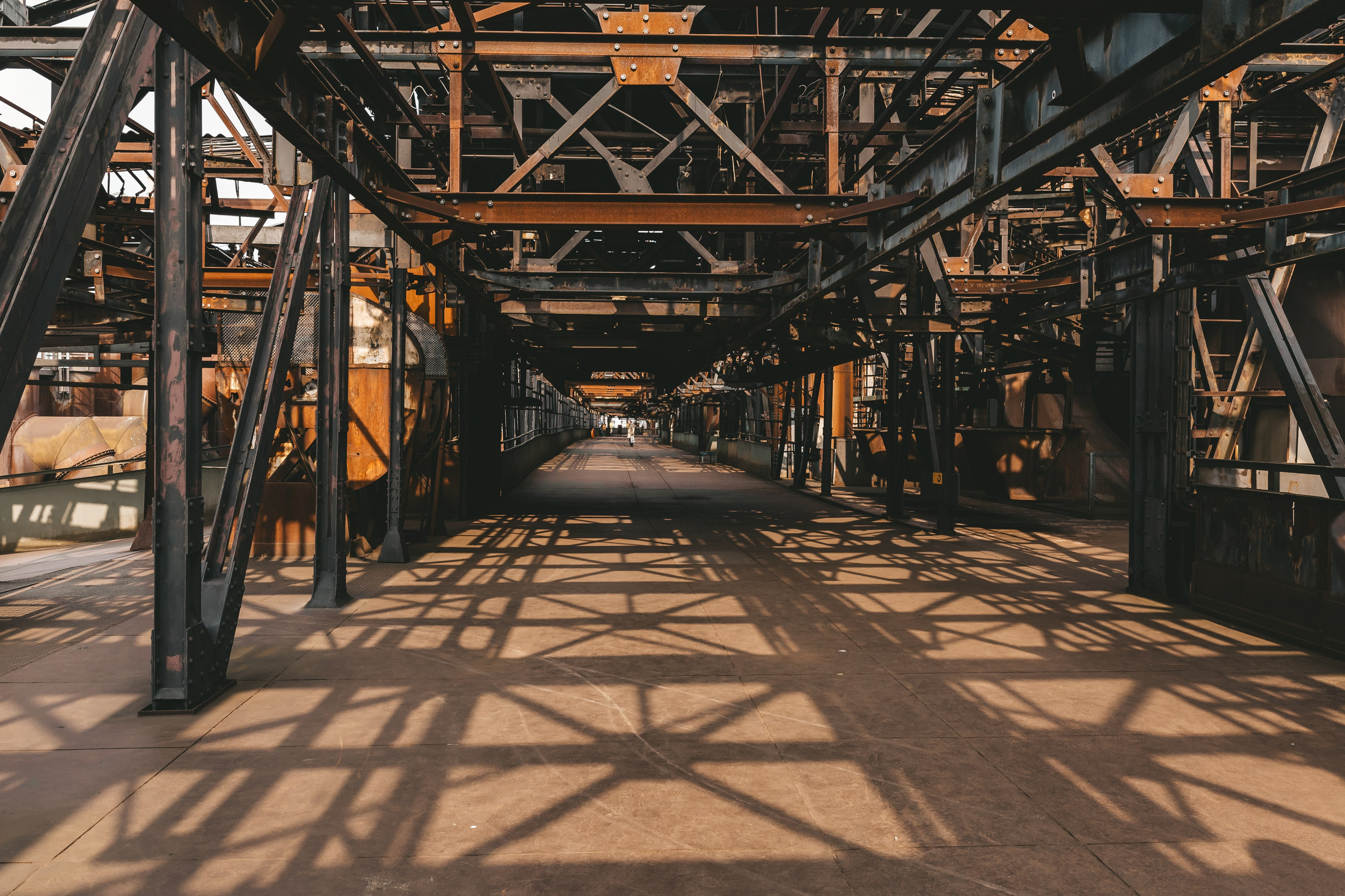 Длинный проход внутри завода с металлическими лестницами и балками.