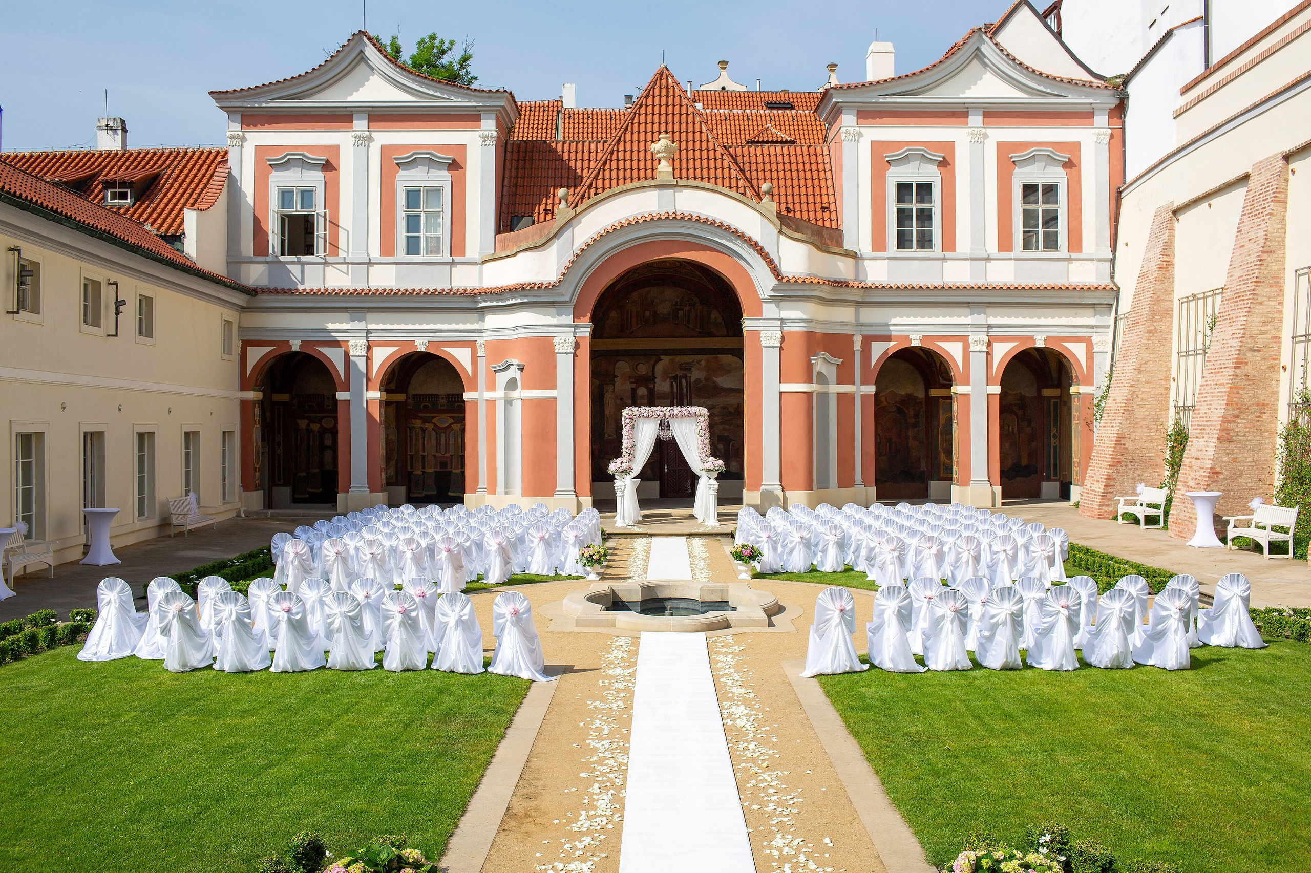A chandelier swings above a floral arch as seating covered in fabric and a festive bow await the arrival of the wedding guests at the Ledebour Garden.