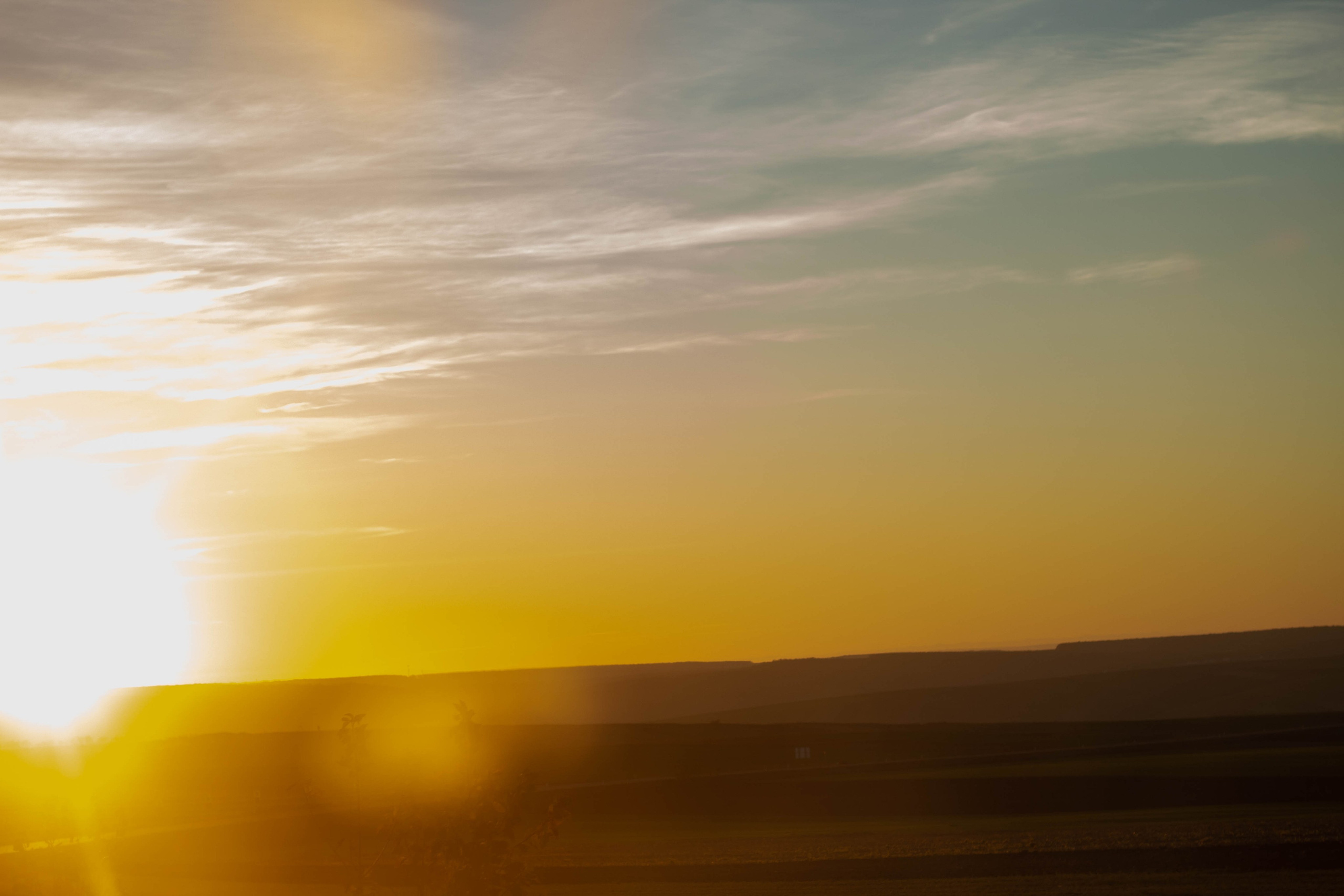 Sunset over distant hills and a wide-open field, golden light filling the sky.