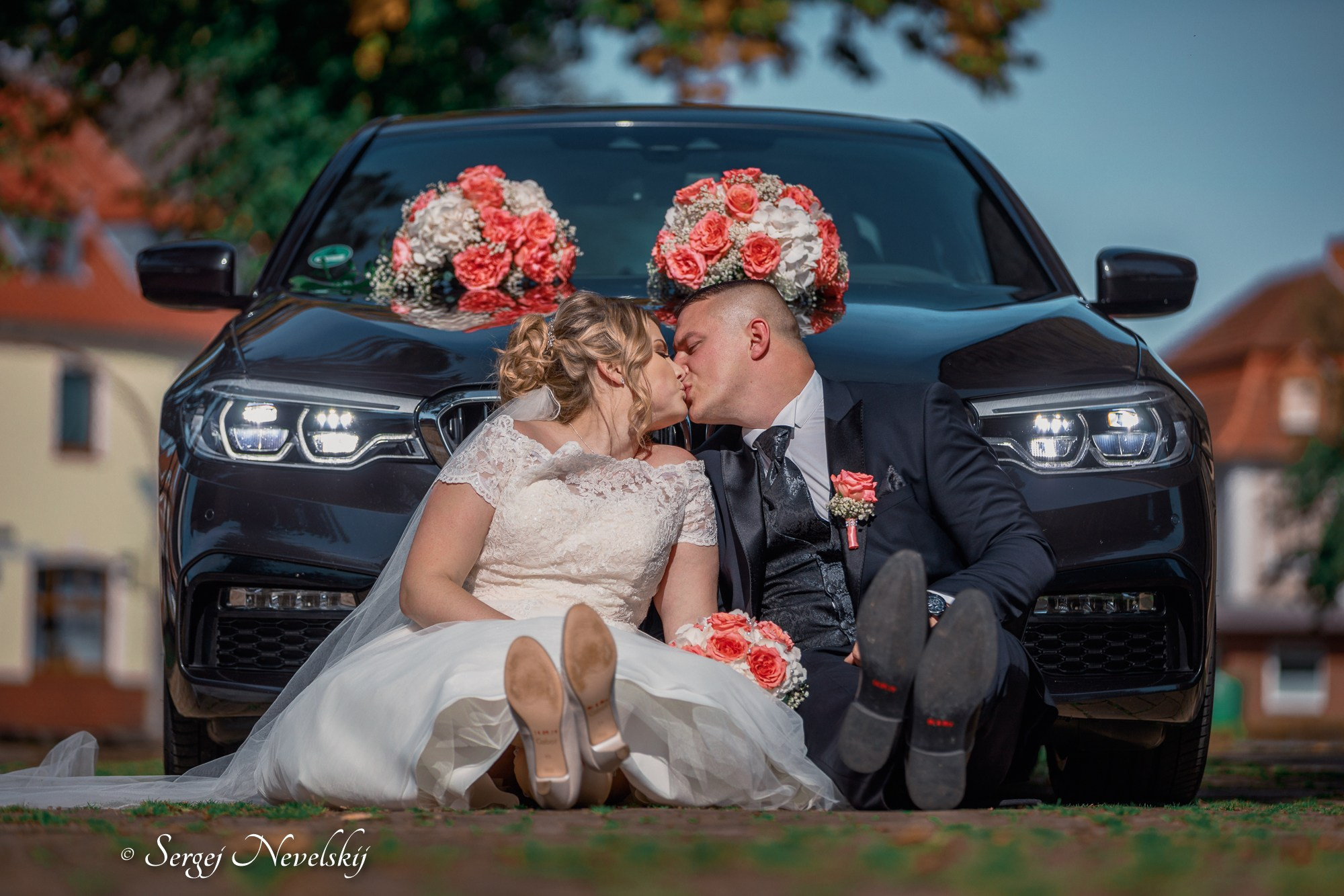 English:Newlyweds sharing a romantic kiss while sitting on the hood of a luxury black BMW decorated with large pink and white rose bouquets. Bride in an elegant off-the-shoulder lace wedding dress with long veil, groom in a classic black suit with matching boutonniere. Playful and stylish wedding portrait full of love and joy. Photo by © Sergej NevelskijРусский:Молодожёны страстно целуются, сидя на капоте чёрного премиального BMW, украшенного большими букетами из розовых и белых роз. Невеста в изящном свадебном платье с открытыми плечами и кружевом, с длинной фатой, жених в классическом чёрном костюме с бутоньеркой. Игривая и стильная свадебная фотография, полная любви и счастья. Фото © Sergej NevelskijDeutsch:Brautpaar küsst sich leidenschaftlich auf der Motorhaube eines schwarzen Luxus-BMWs, der mit großen rosé-weißen Rosensträußen dekoriert ist. Braut im eleganten schulterfreien Spitzenbrautkleid mit langem Schleier, Bräutigam im klassischen schwarzen Anzug mit passendem Anstecker. Verspieltes und stilvolles Hochzeitsporträt voller Liebe und Freude. Foto © Sergej Nevelskij