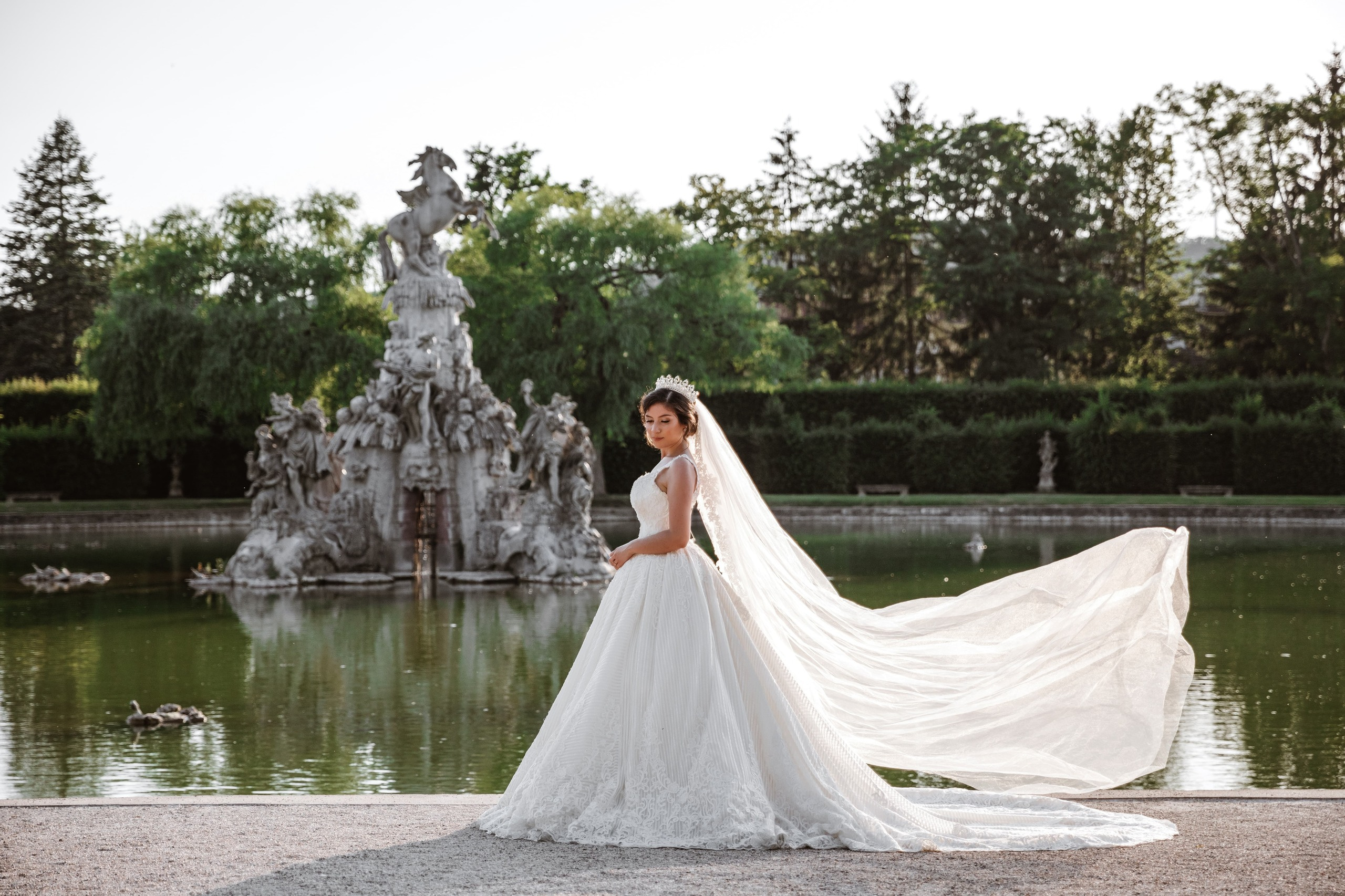 Braut steht am Brunnen, der Schleier weht im Wind im Schloss Veitshöchheim.