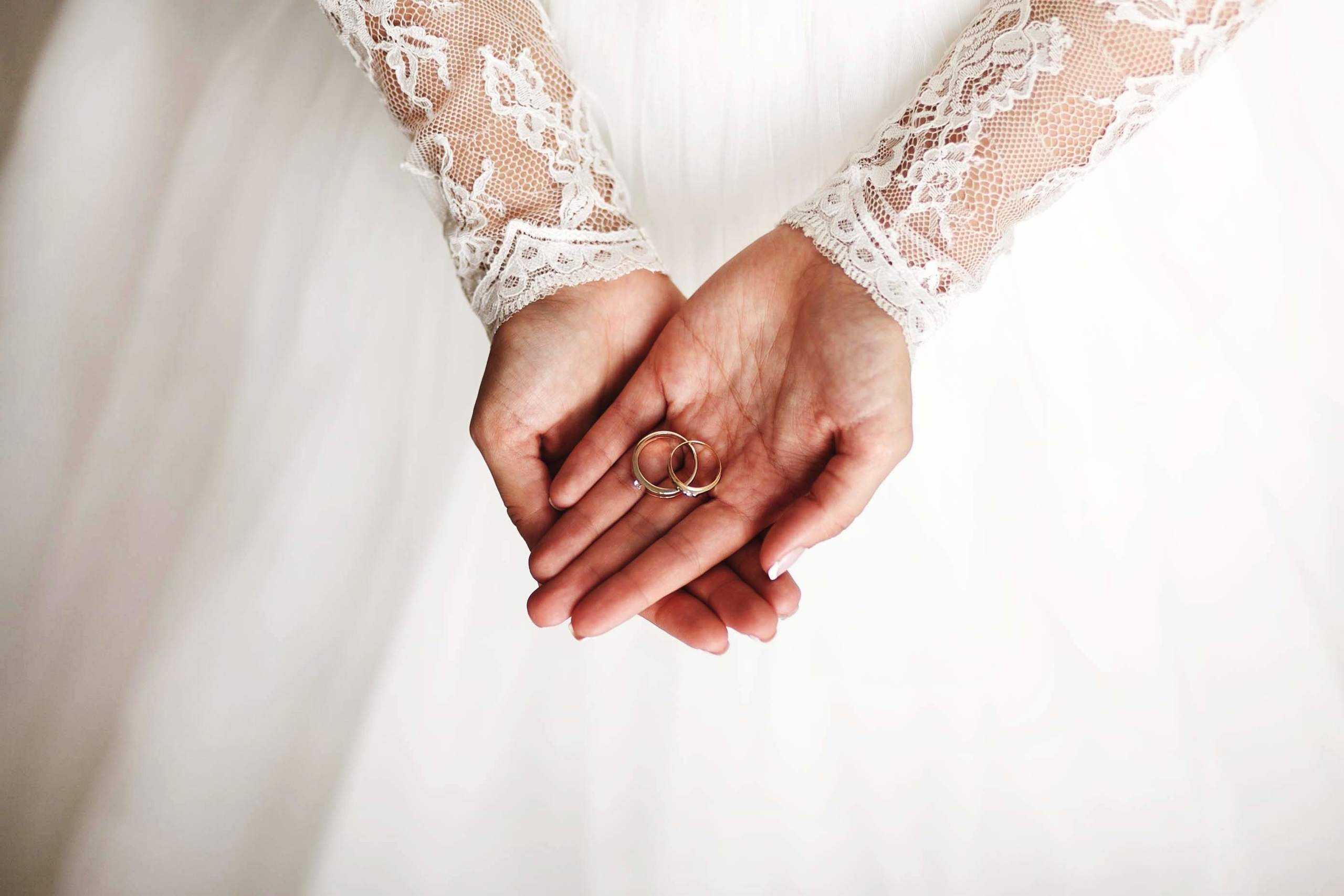 Eheringe liegen auf der Hand der Braut, Spitzenärmel ihres Hochzeitskleides sichtbar.