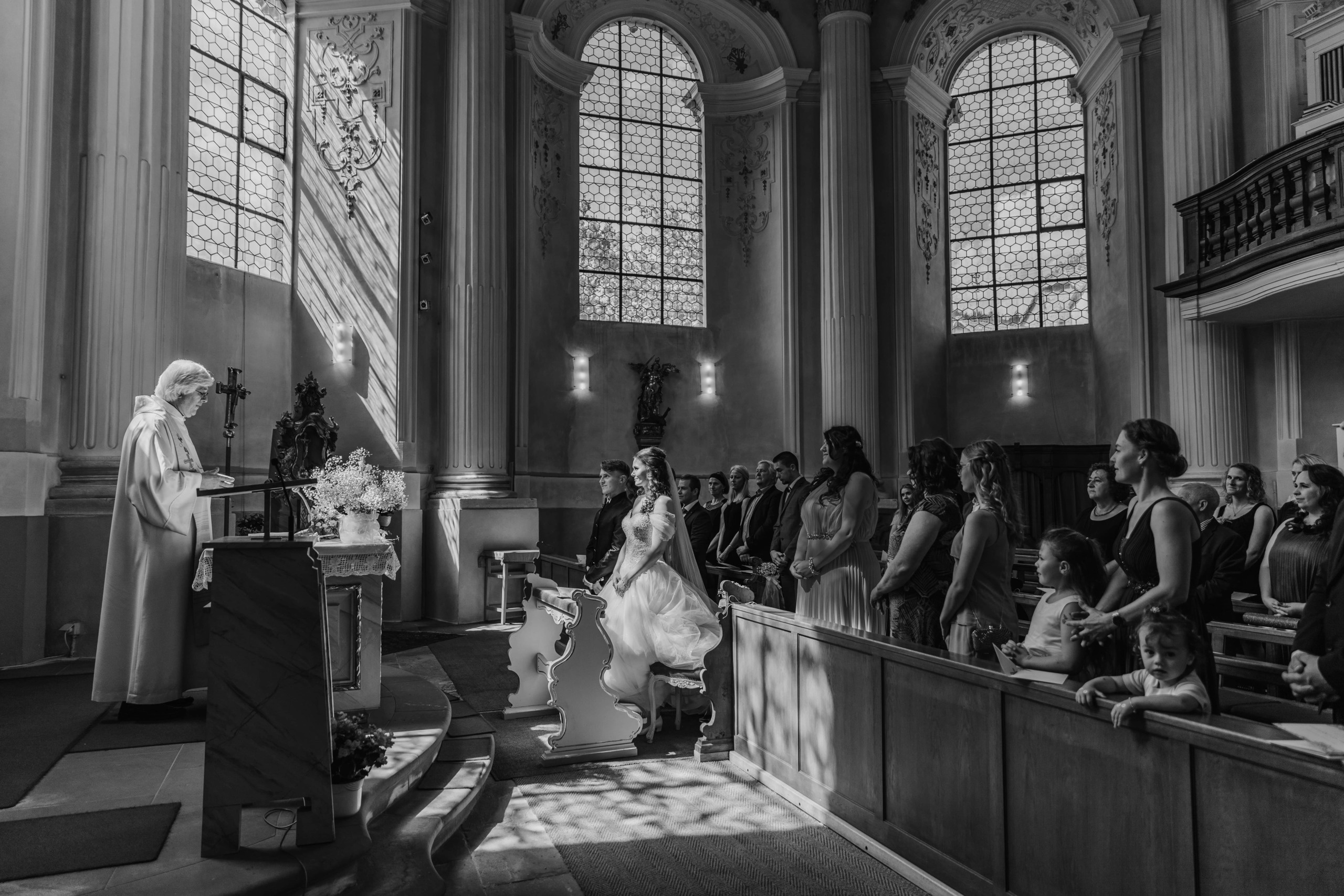 Das Brautpaar steht vor dem Altar in der beeindruckenden Kulisse der Kirche, von Sonnenstrahlen durchflutet.