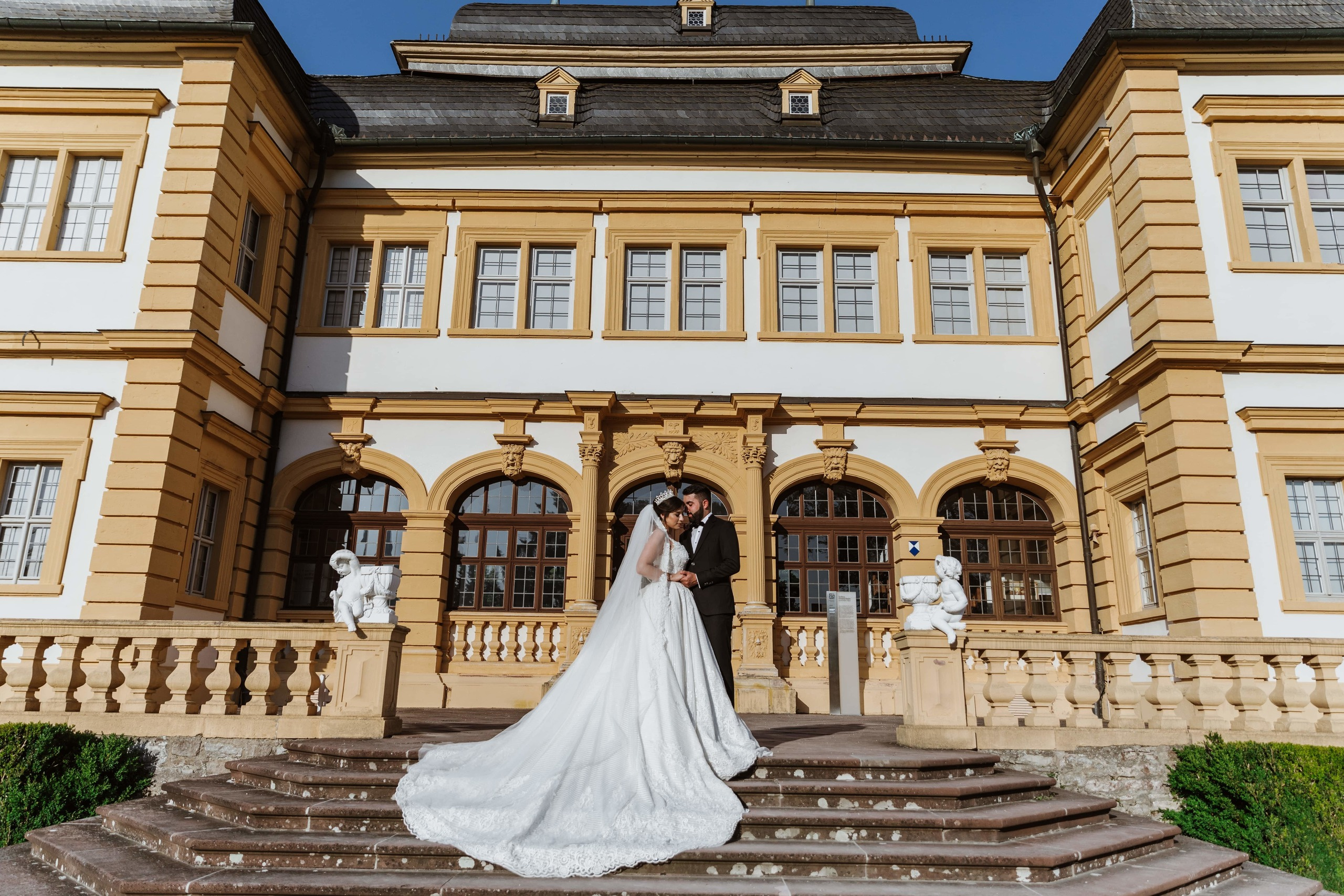 Bräutigam und Braut stehen auf der Treppe vor Schloss Veitshöchheim.