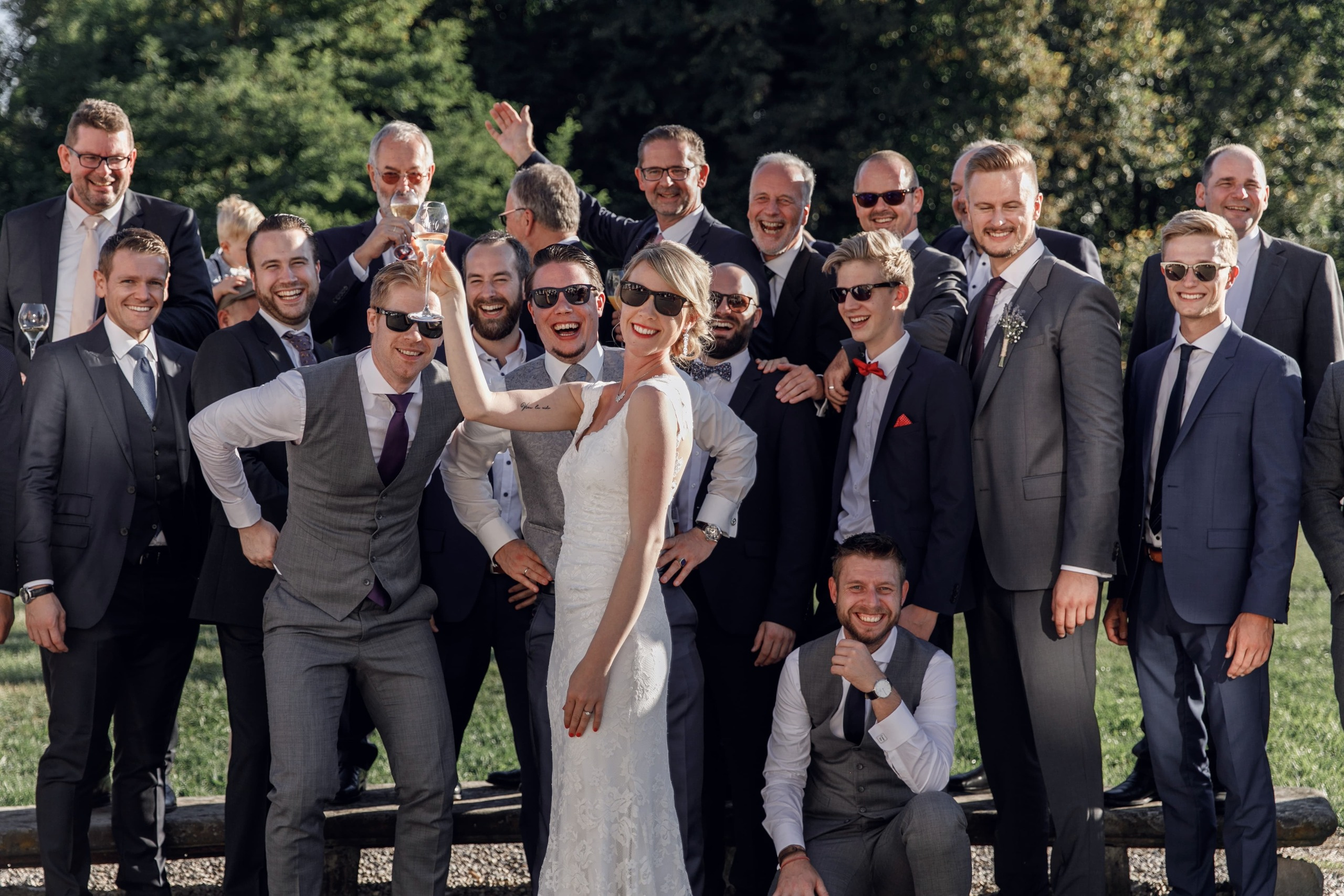 Freunde des Bräutigams blicken lächelnd auf die Braut mit Champagnerglas.