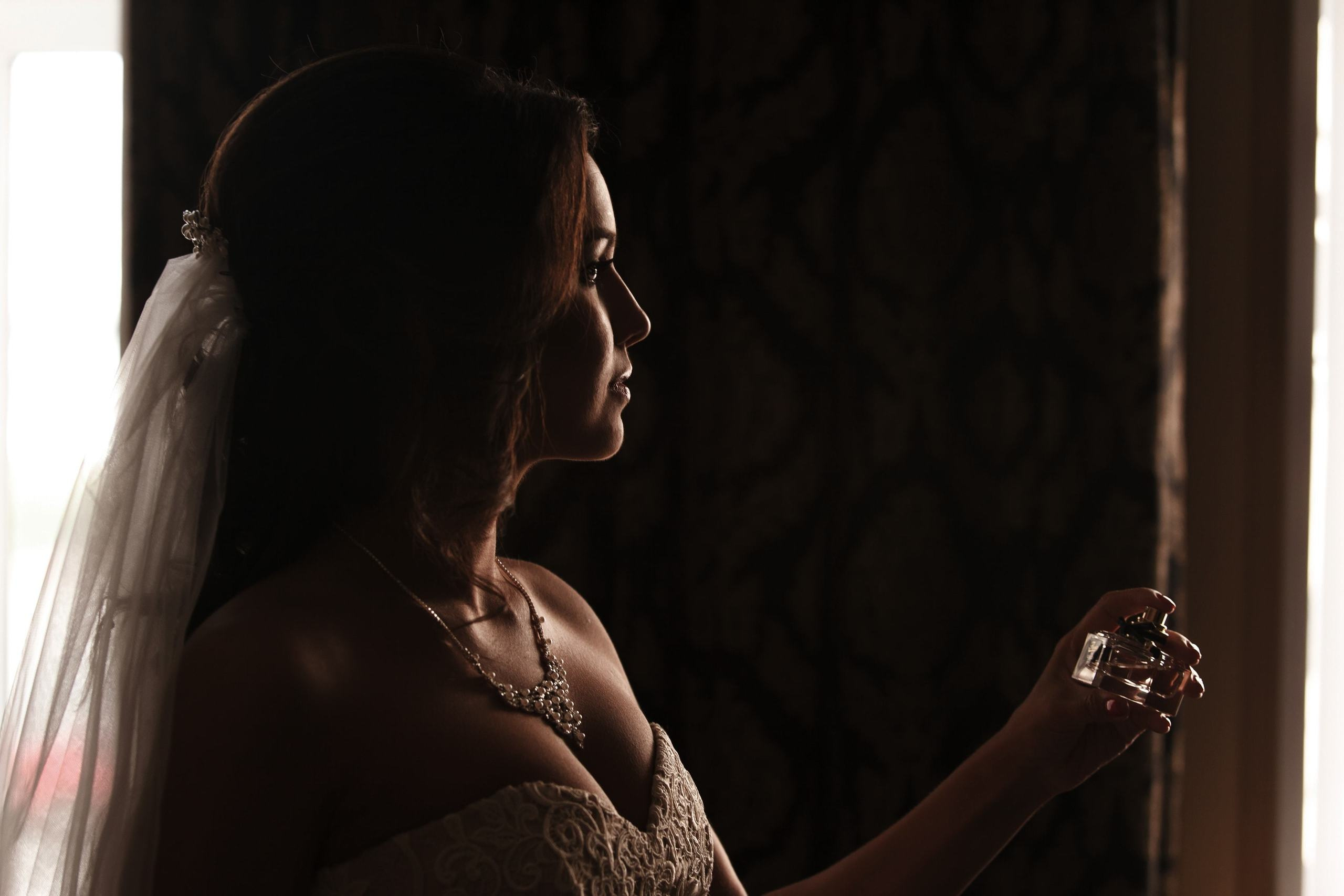 Die Braut sprüht Parfüm, während sie im Profil zu uns steht.