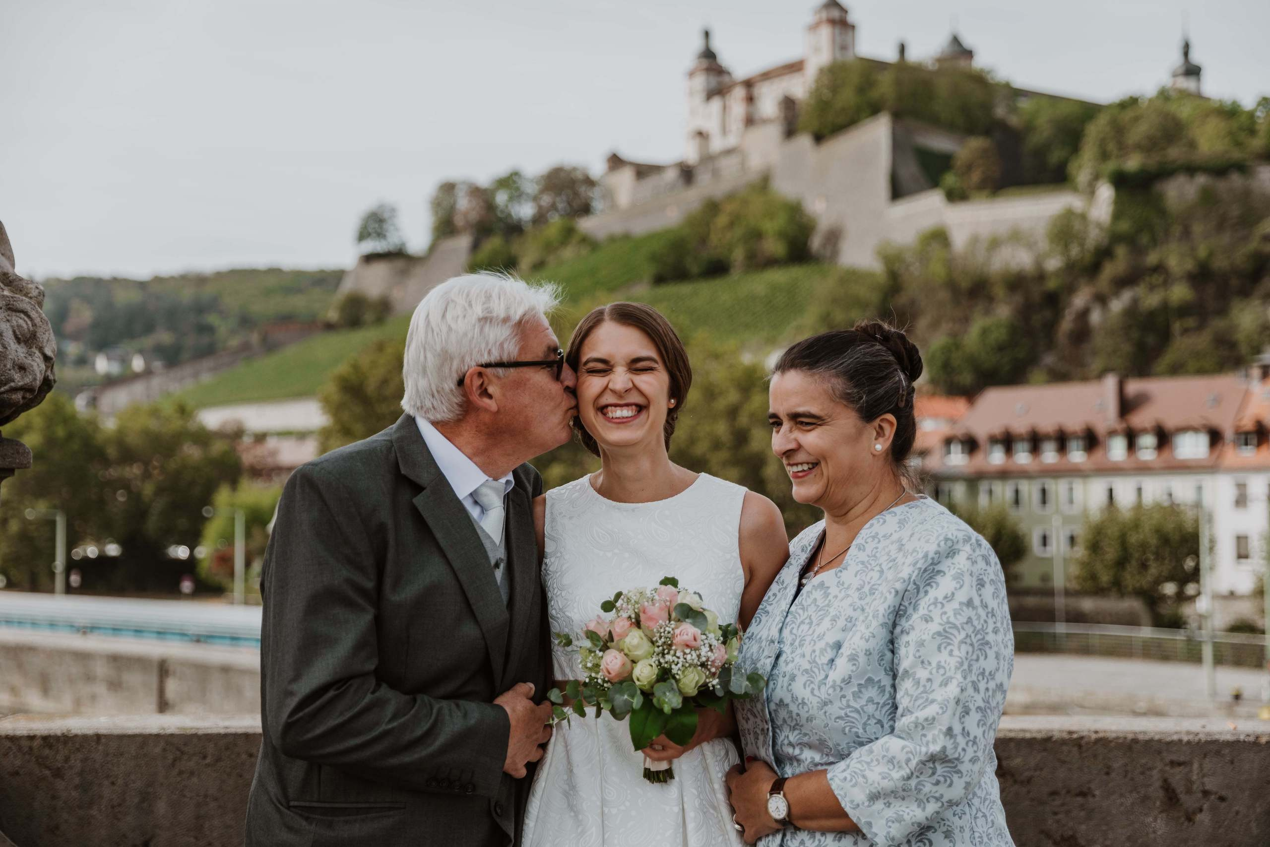 Eltern umarmen die Braut auf der Alten Mainbrücke in Würzburg.