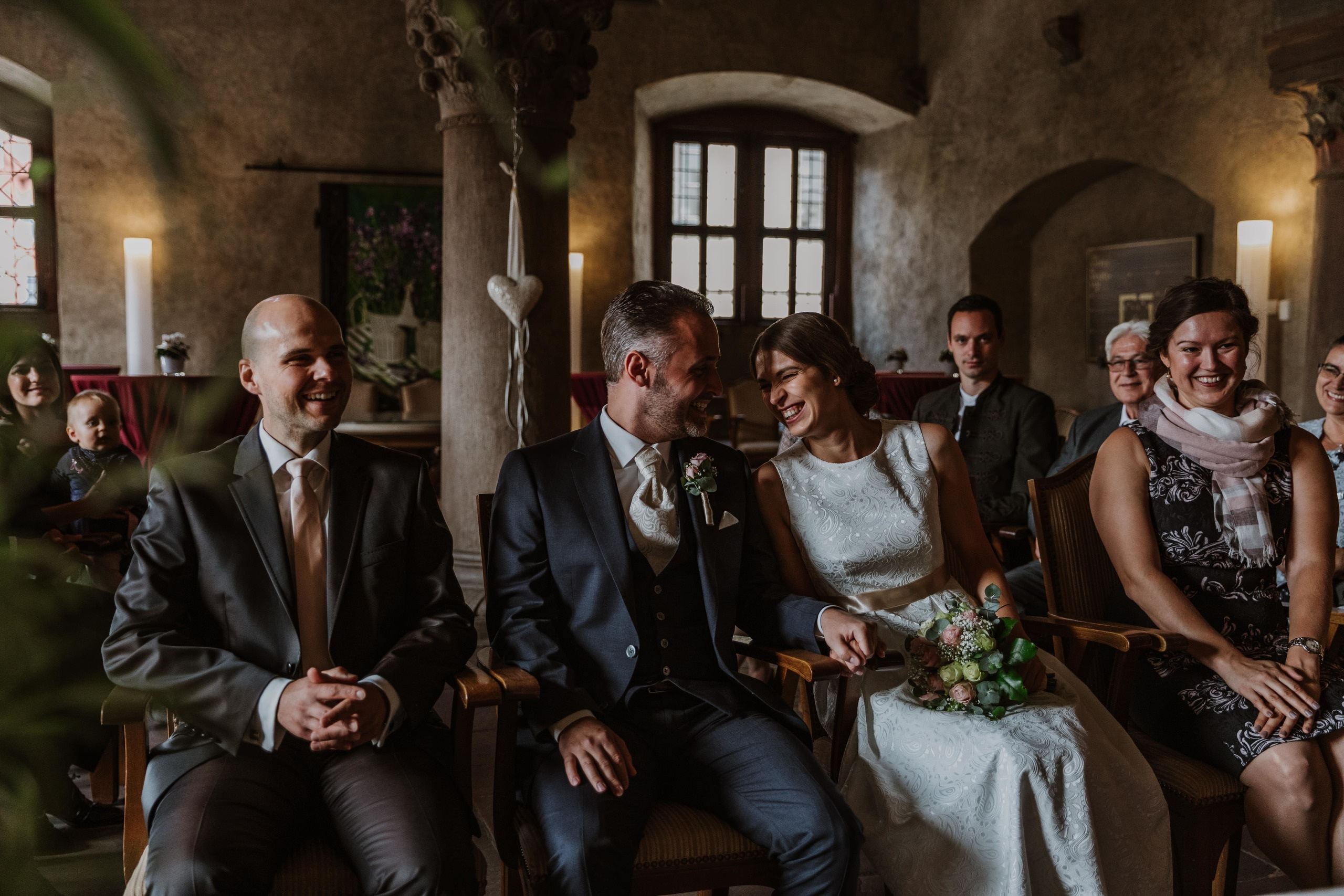 Bräutigam, Braut und Trauzeugen lachen während der Zeremonie im Wenzelsaal im Grafeneckart-Turm im Würzburg.
