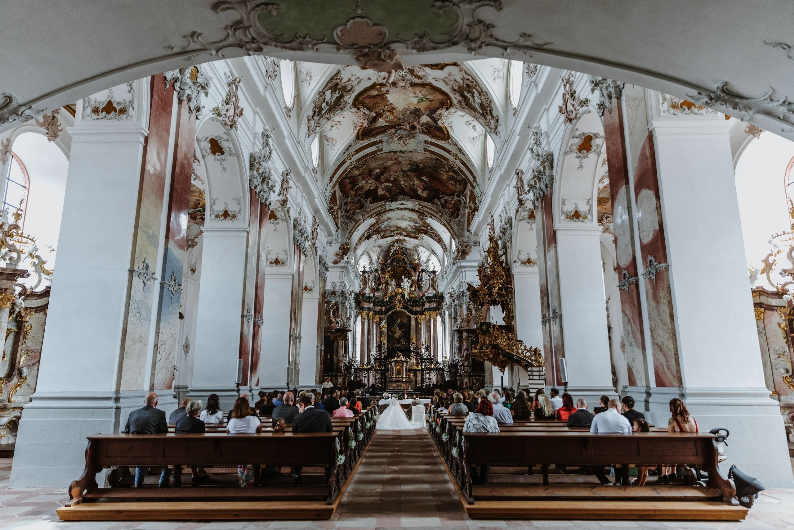 Panorama einer prächtigen Abteikirche Amorbach, im Hintergrund sind die Rücken von der Hochzeitsgäste und des Brautpaares zu sehen.