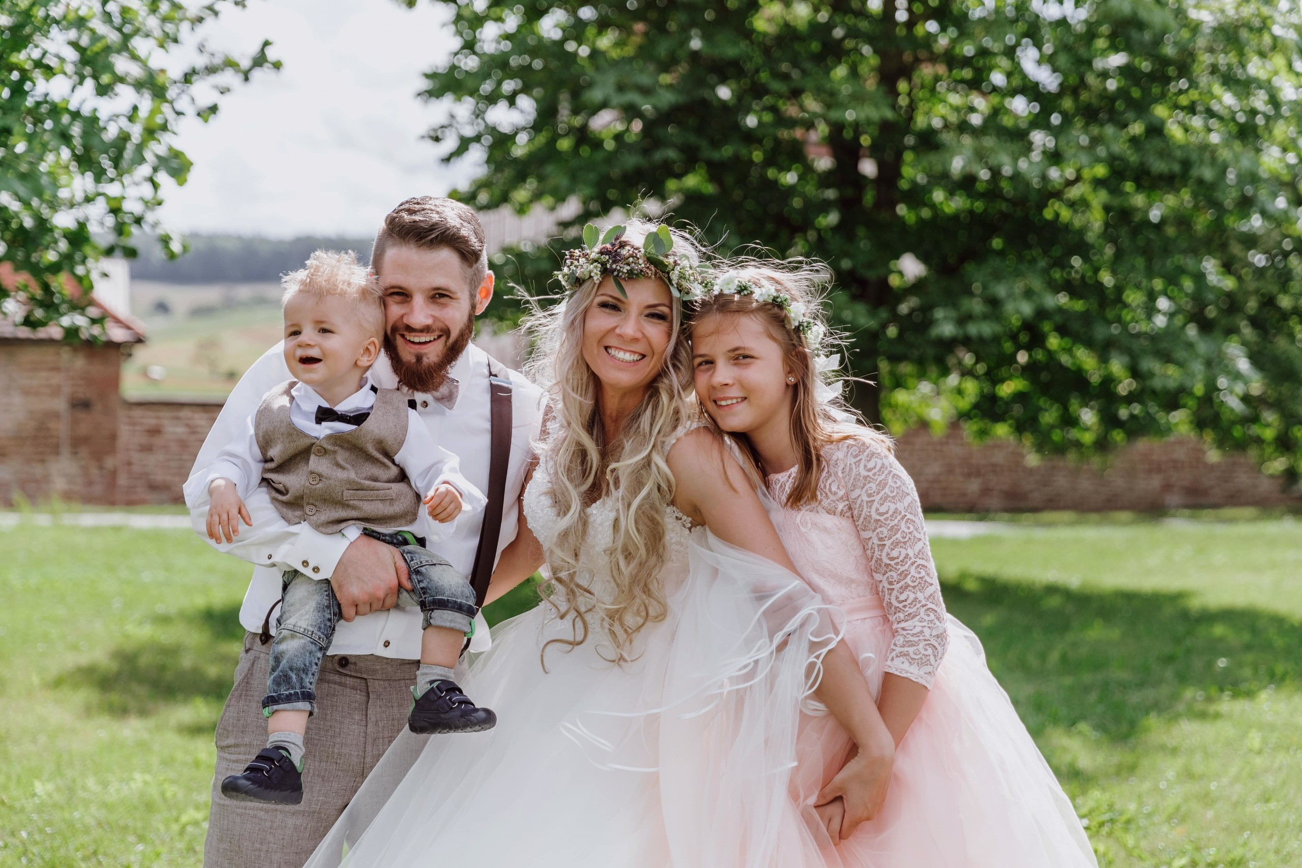 Der Bräutigam, die Braut und ihre Kinder lachen und schauen in die Kamera, während sie auf einer grünen Wiese im Gut Rosshof stehen.