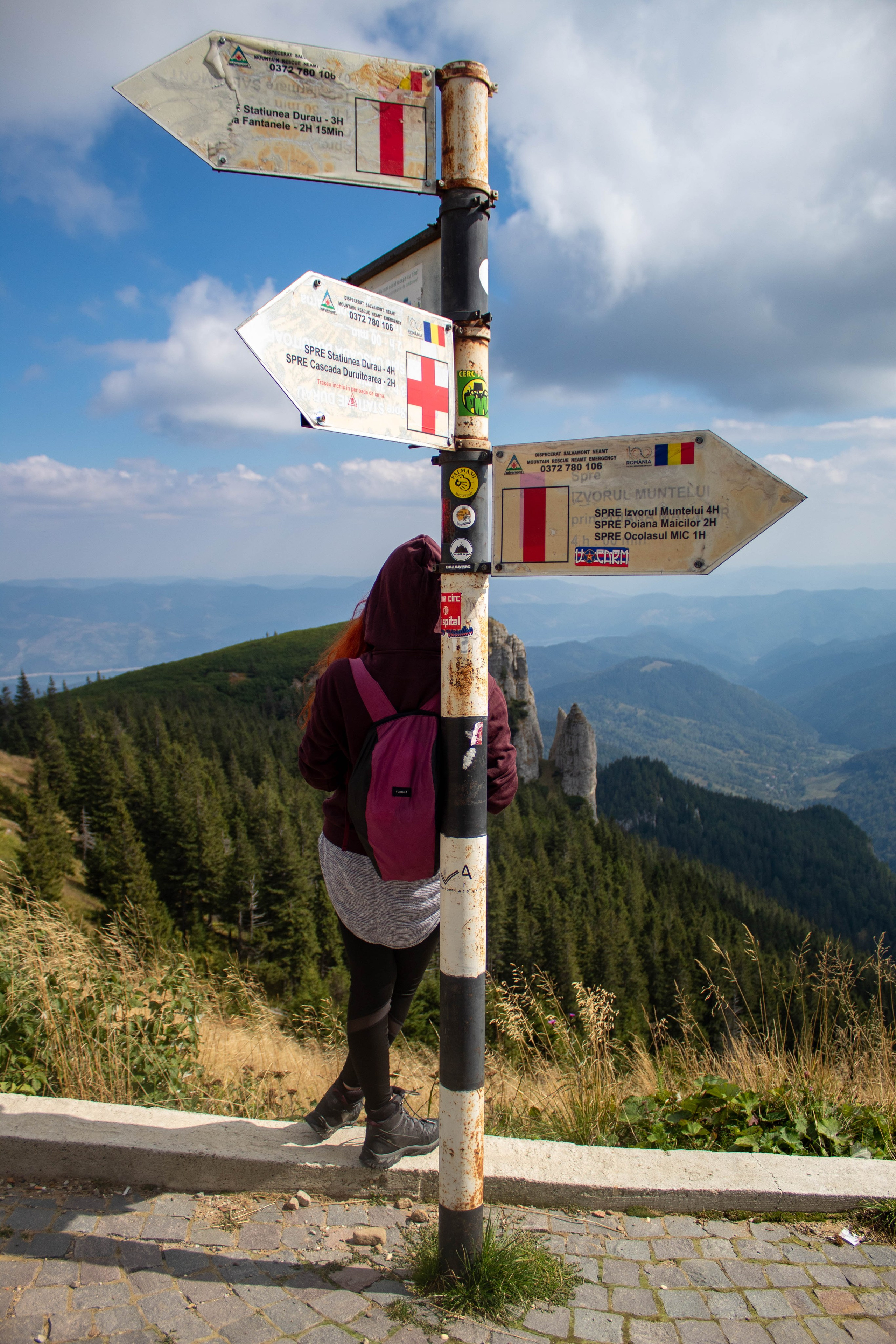Person standing at a wooden mountain trail signpost on a sunny day in the Carpathians.