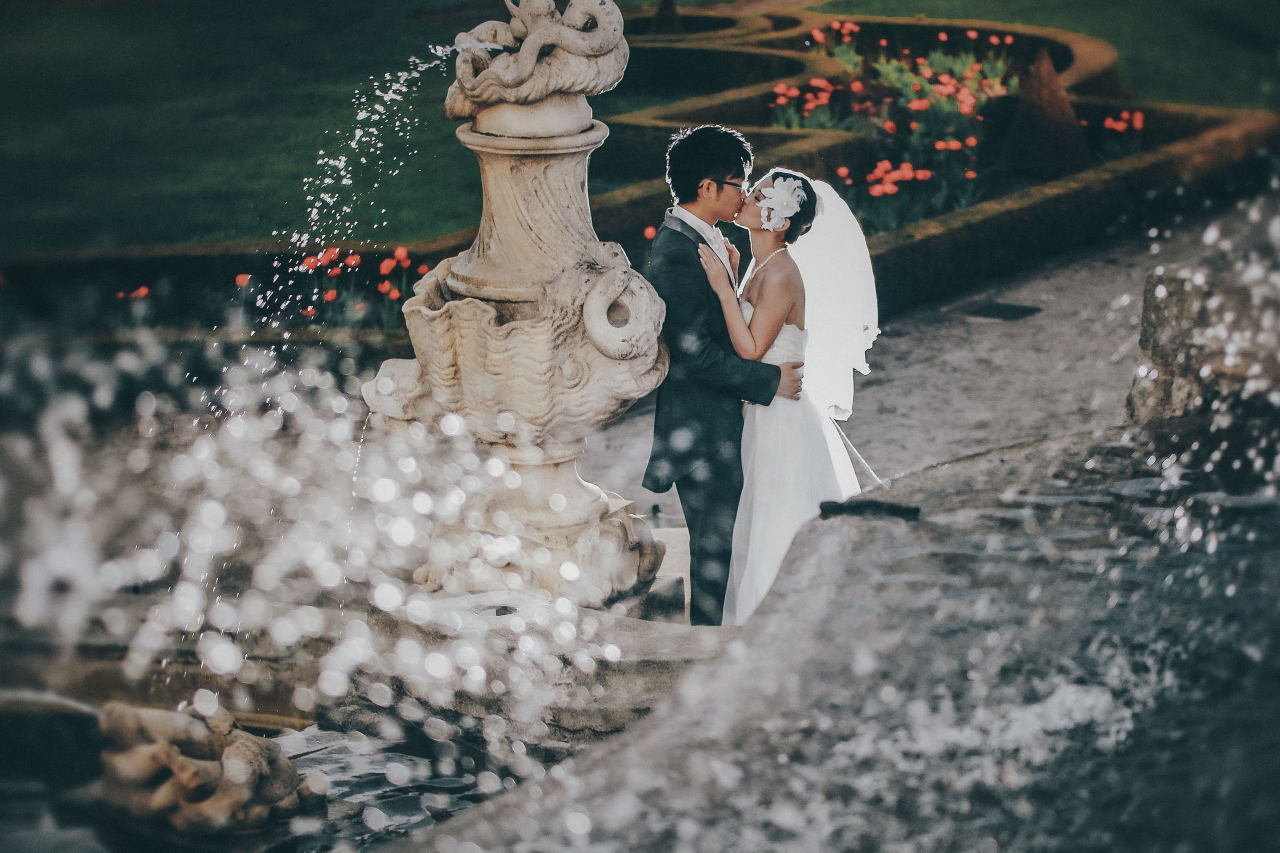 Cheerful Hong Kong couple embracing with water droplets around them by the fountains at Cesky Krumlov Castle.