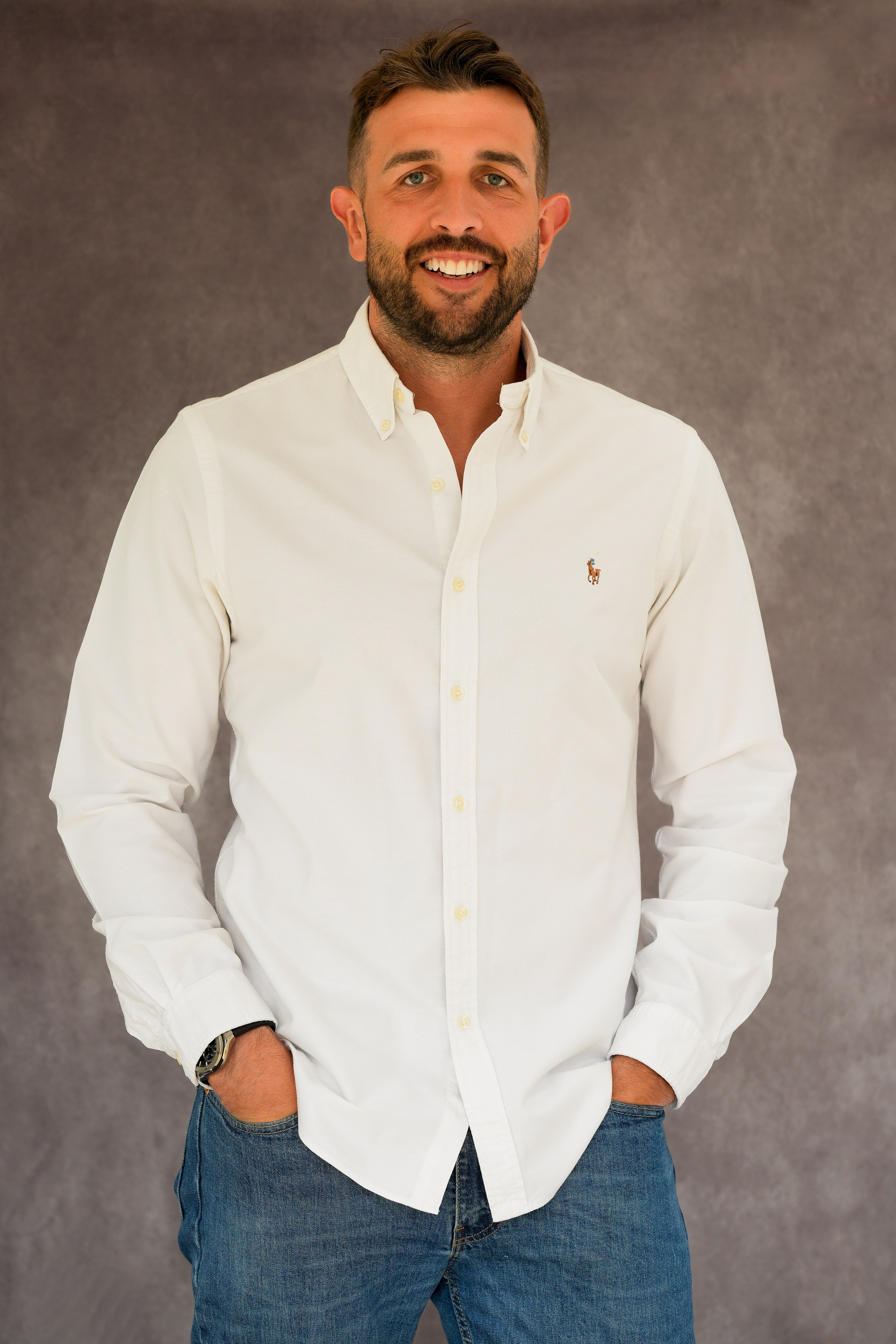 Professional headshot in Solihull of young man in a crisp white shirt, smiling confidently against an artistic studio background. 