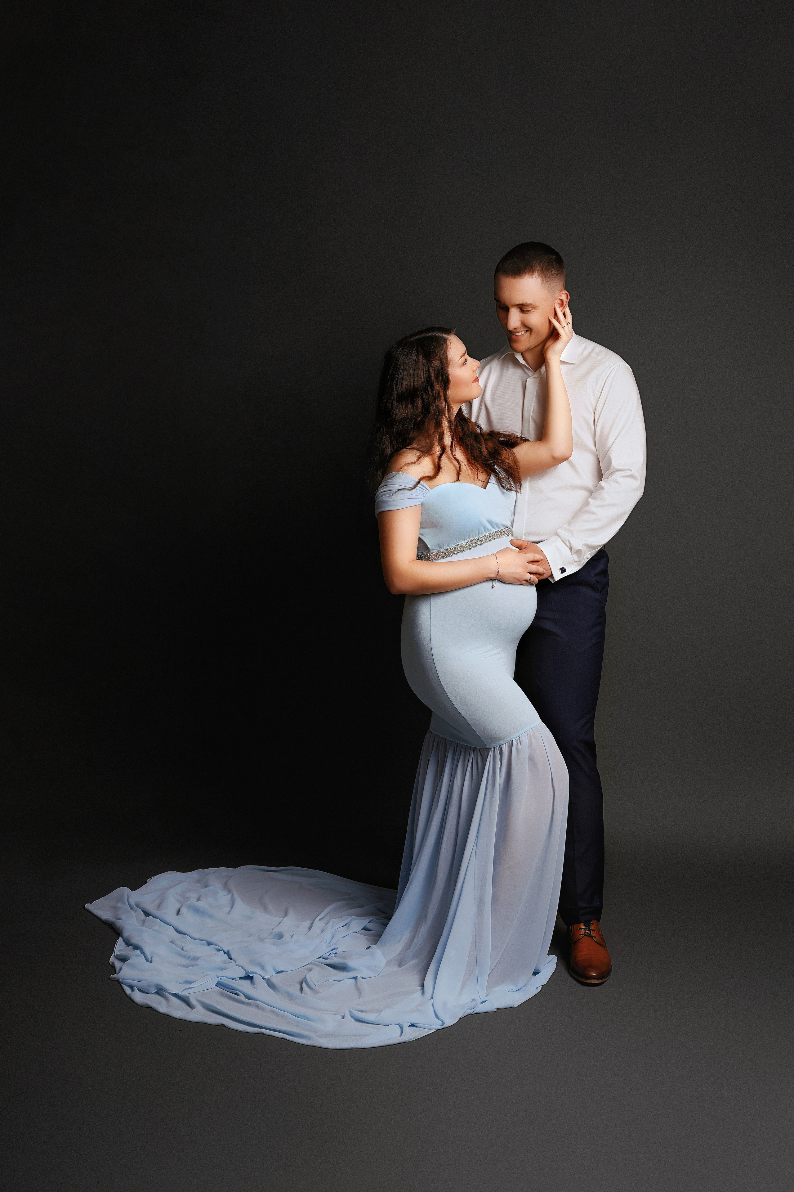 Schwangere mit Partner im hellblauen Schleppenkleid im Fotostudio