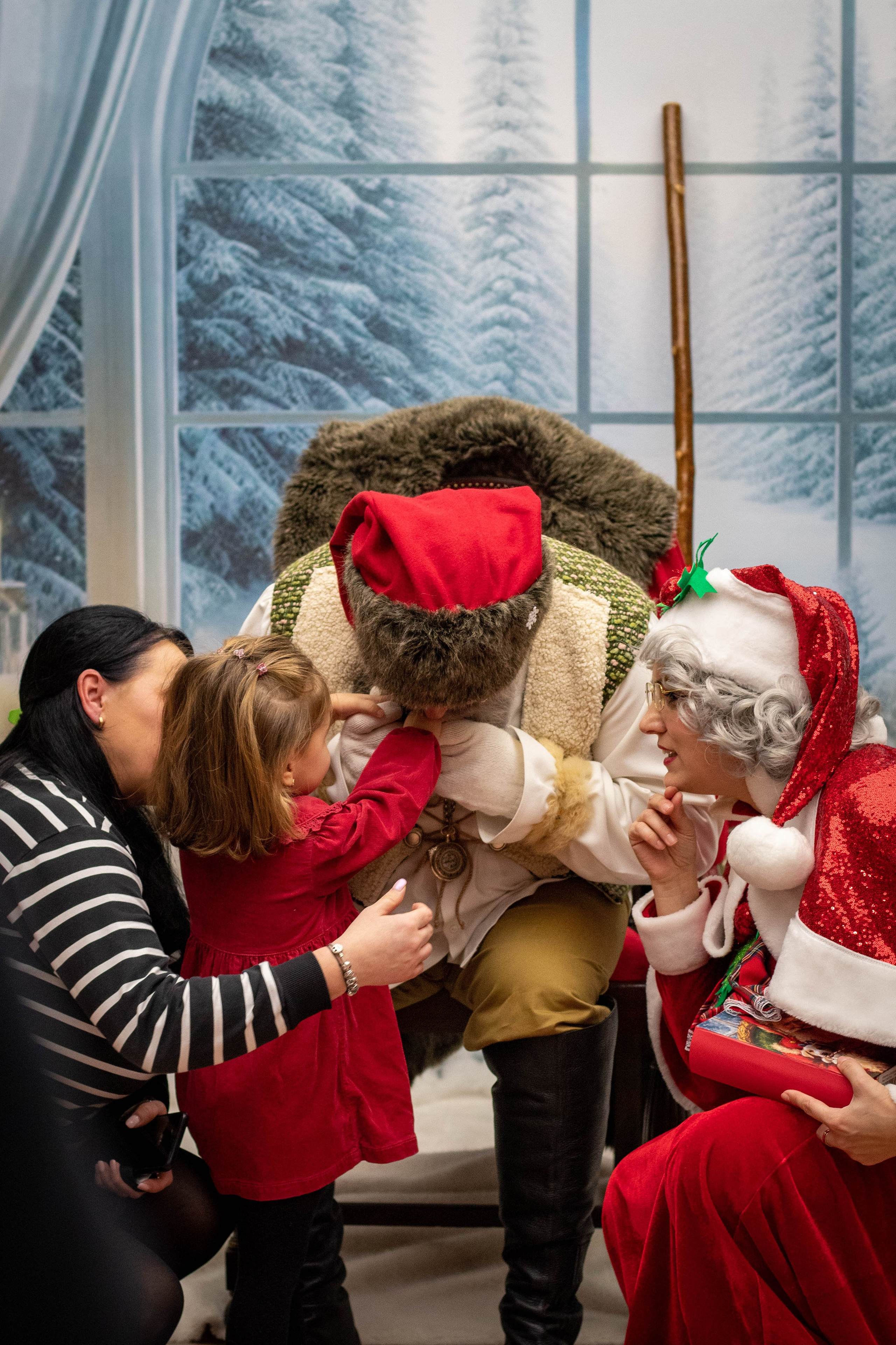 Santa Claus sitting with two smiling children indoors during a holiday event.