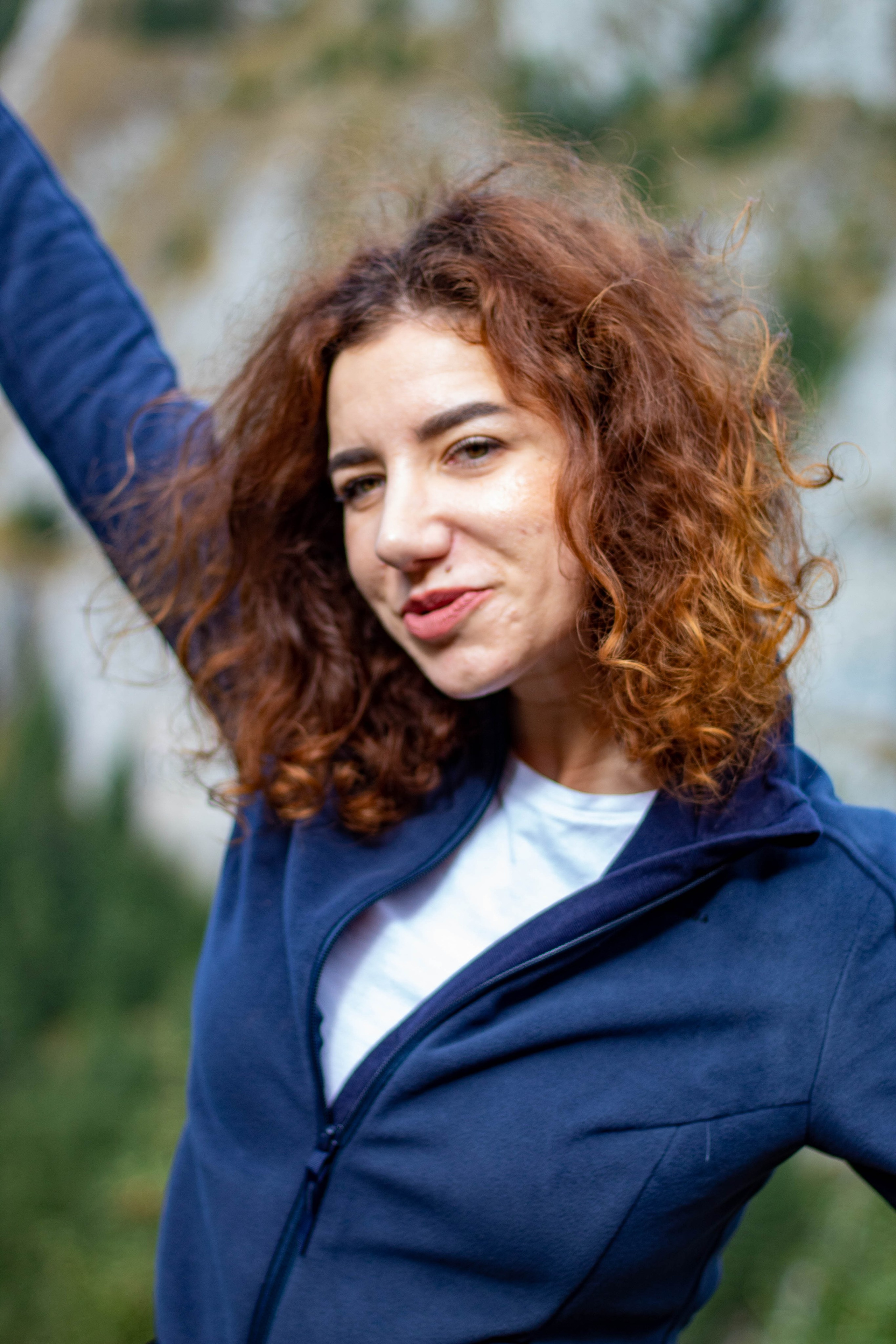 Portrait of a smiling red-haired woman in a blue blazer raising her arm in a confident pose.