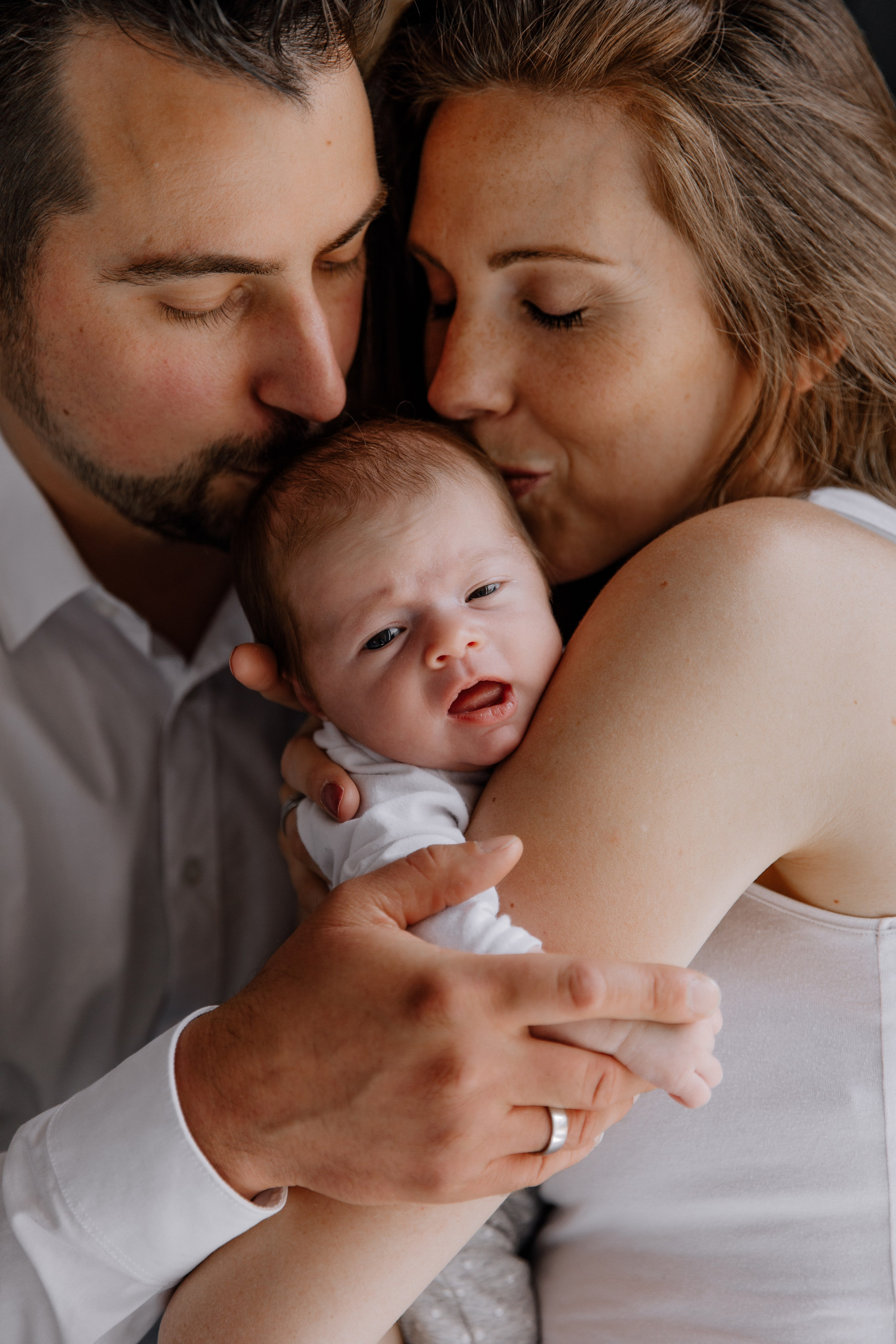 Mama und Papa küssen ihr Baby sanft auf den Kopf.