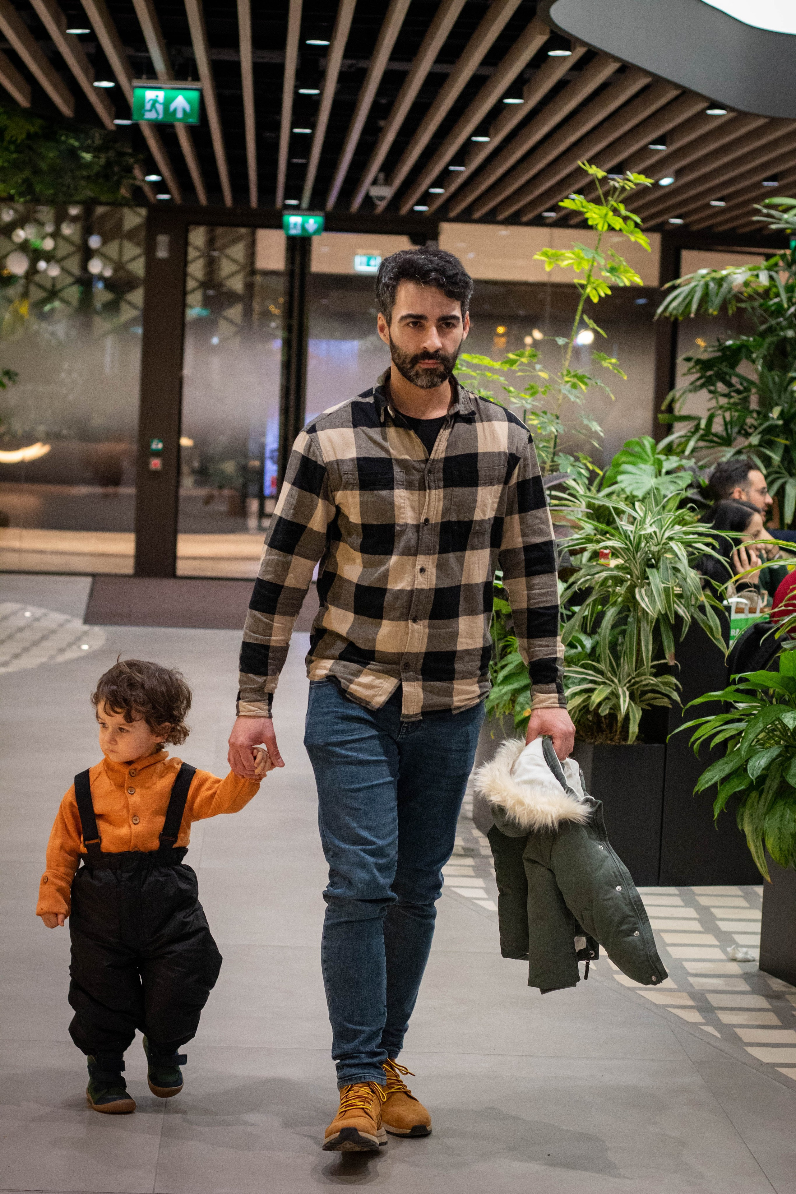 Father and son walking hand-in-hand on a paved path in matching plaid shirts.