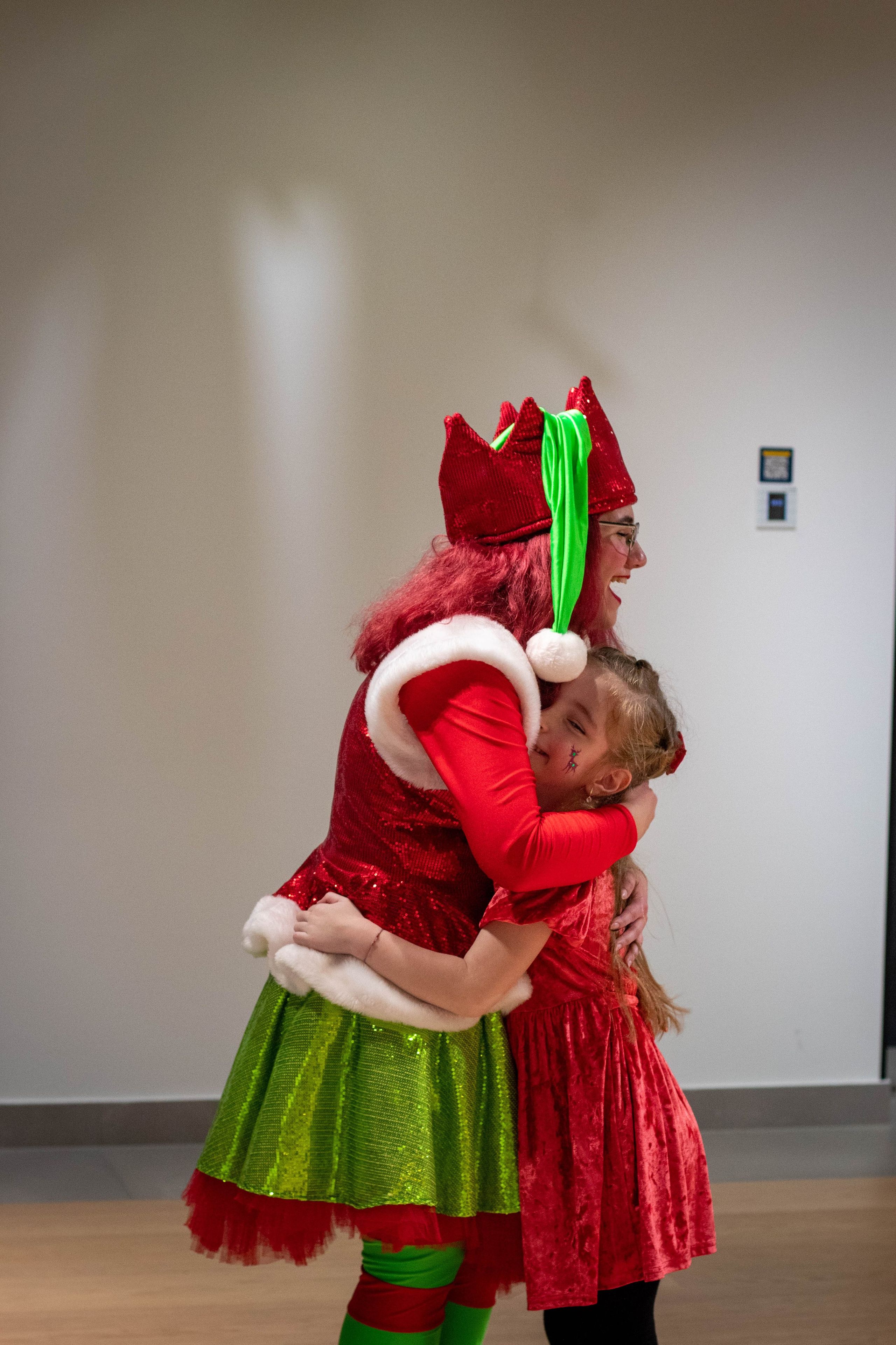 Performer dressed as a holiday elf posing indoors in festive green and red costume.