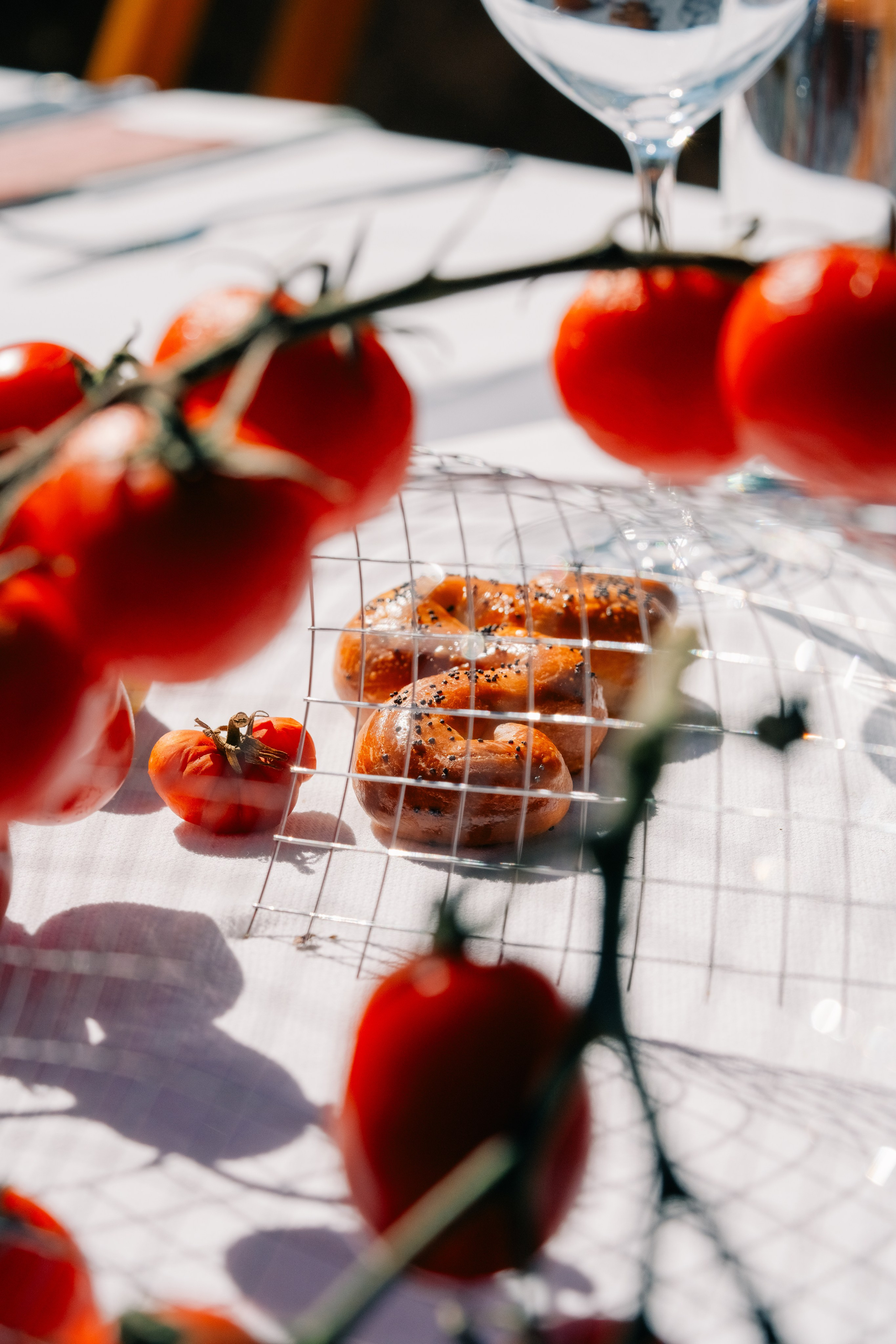 Close-up de tomates frescos e pretzel numa mesa ao ar livre iluminada pelo sol. Grande plano artístico de tomates frescos e um pretzel numa mesa de jantar ao ar livre iluminada pelo sol, criando uma cena vibrante e apetitosa.
