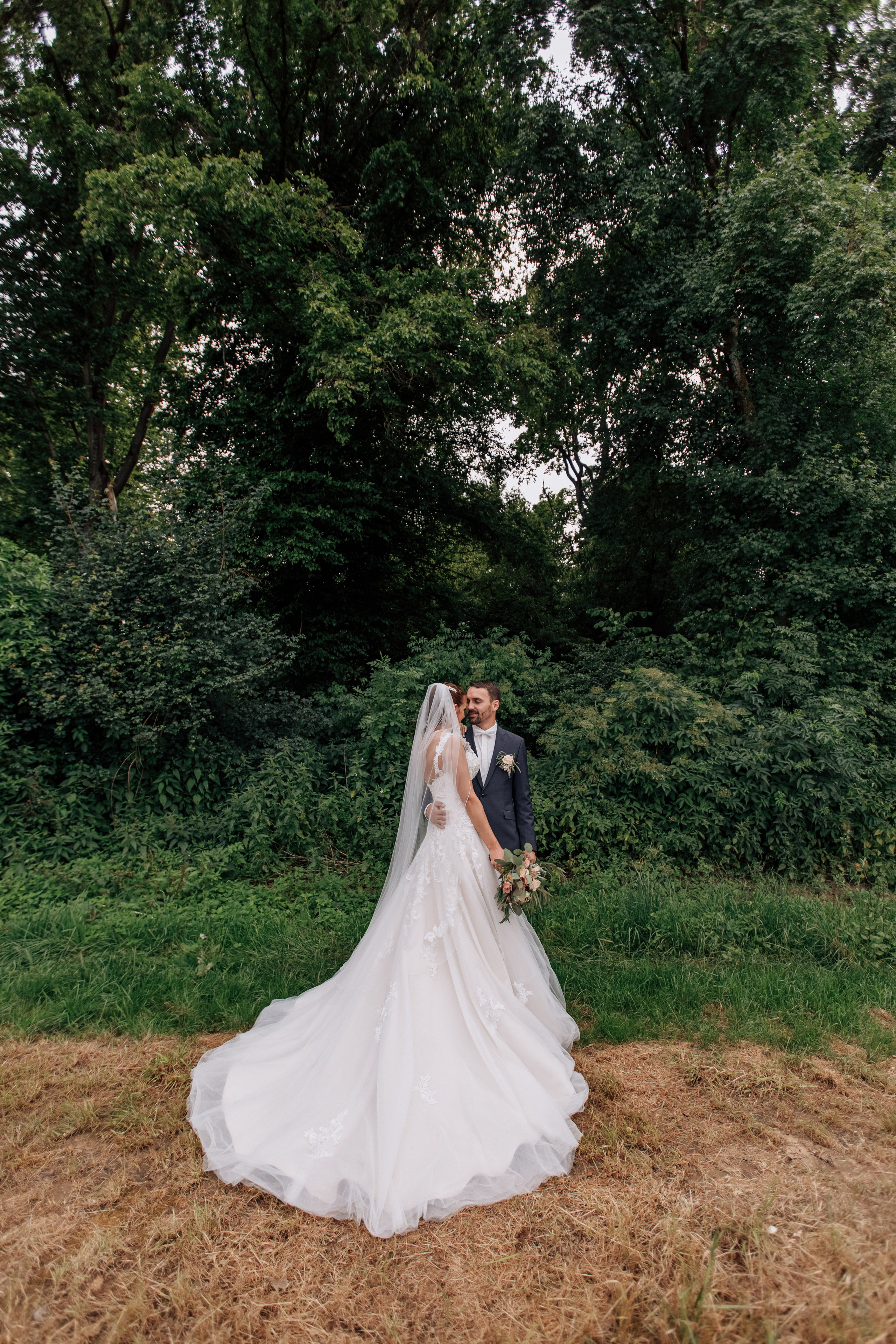 Bräutigam umarmt die Braut, der beeindruckende Schlepptail ihres eleganten Kleides ist sichtbar.