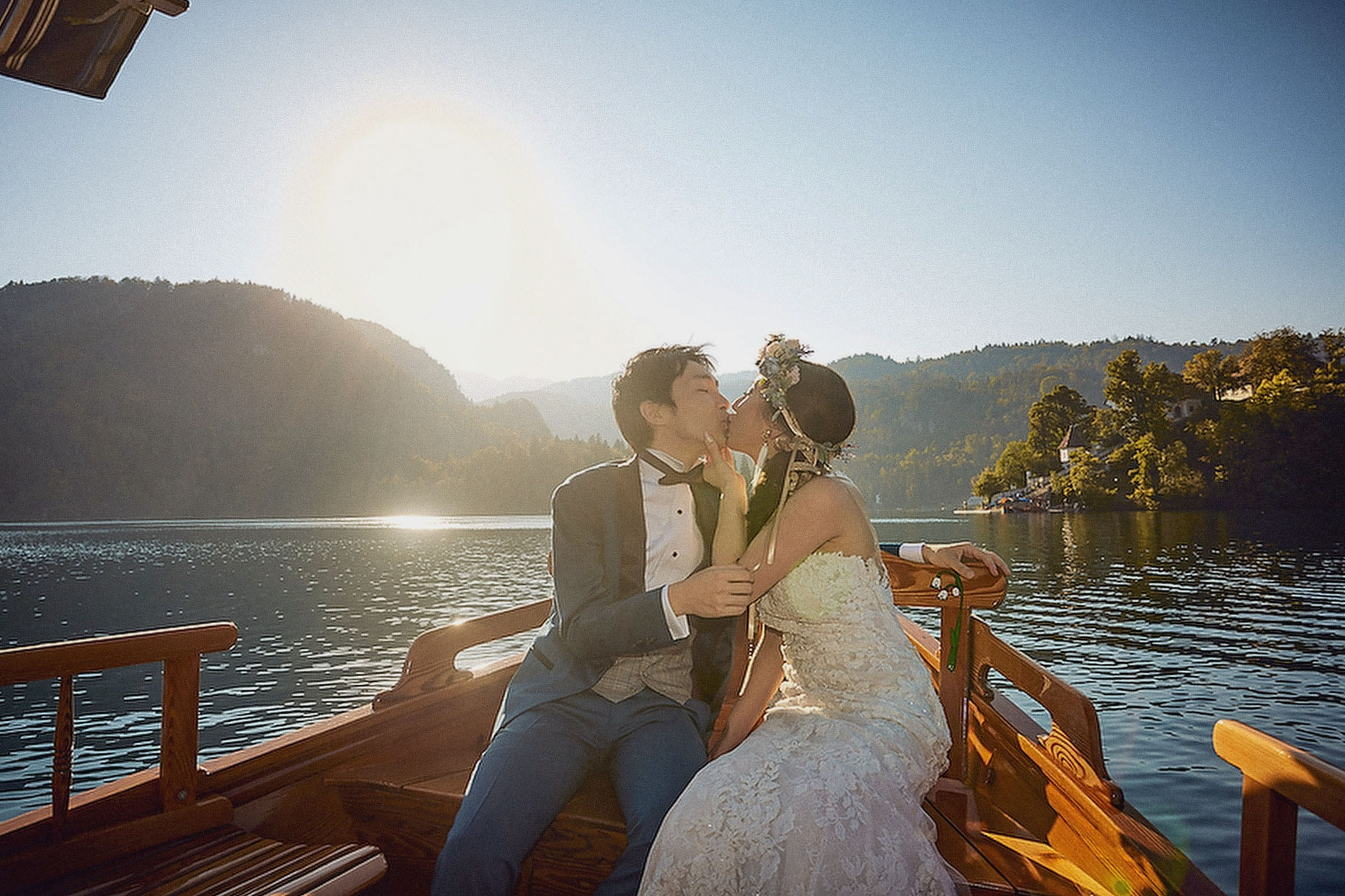 Japanese newlyweds in formal wedding attire cherish their private time aboard a boat as the sun is seen in the sky behind them.