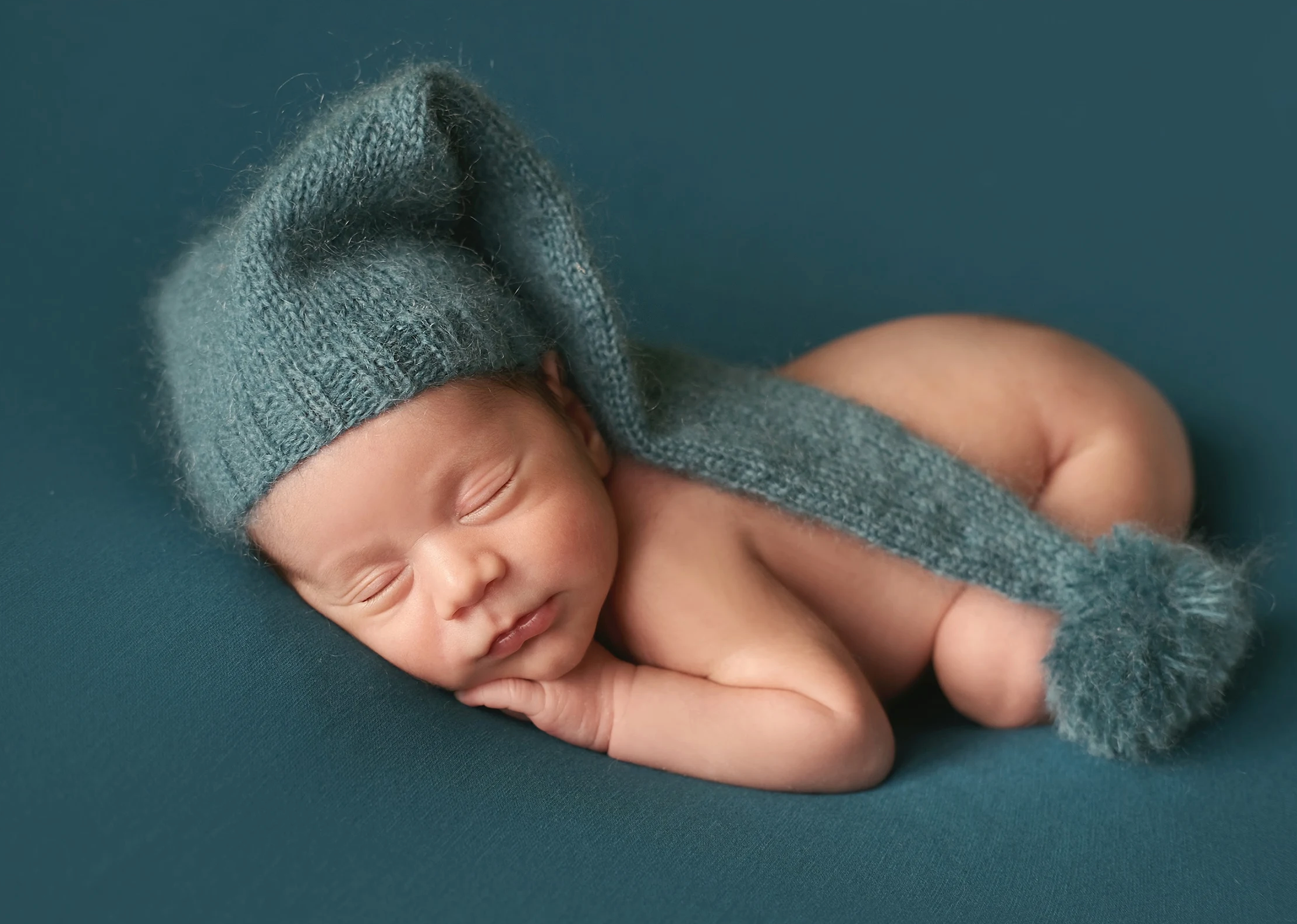 Newborn baby boy sleeping on tummy in knitted nightcap