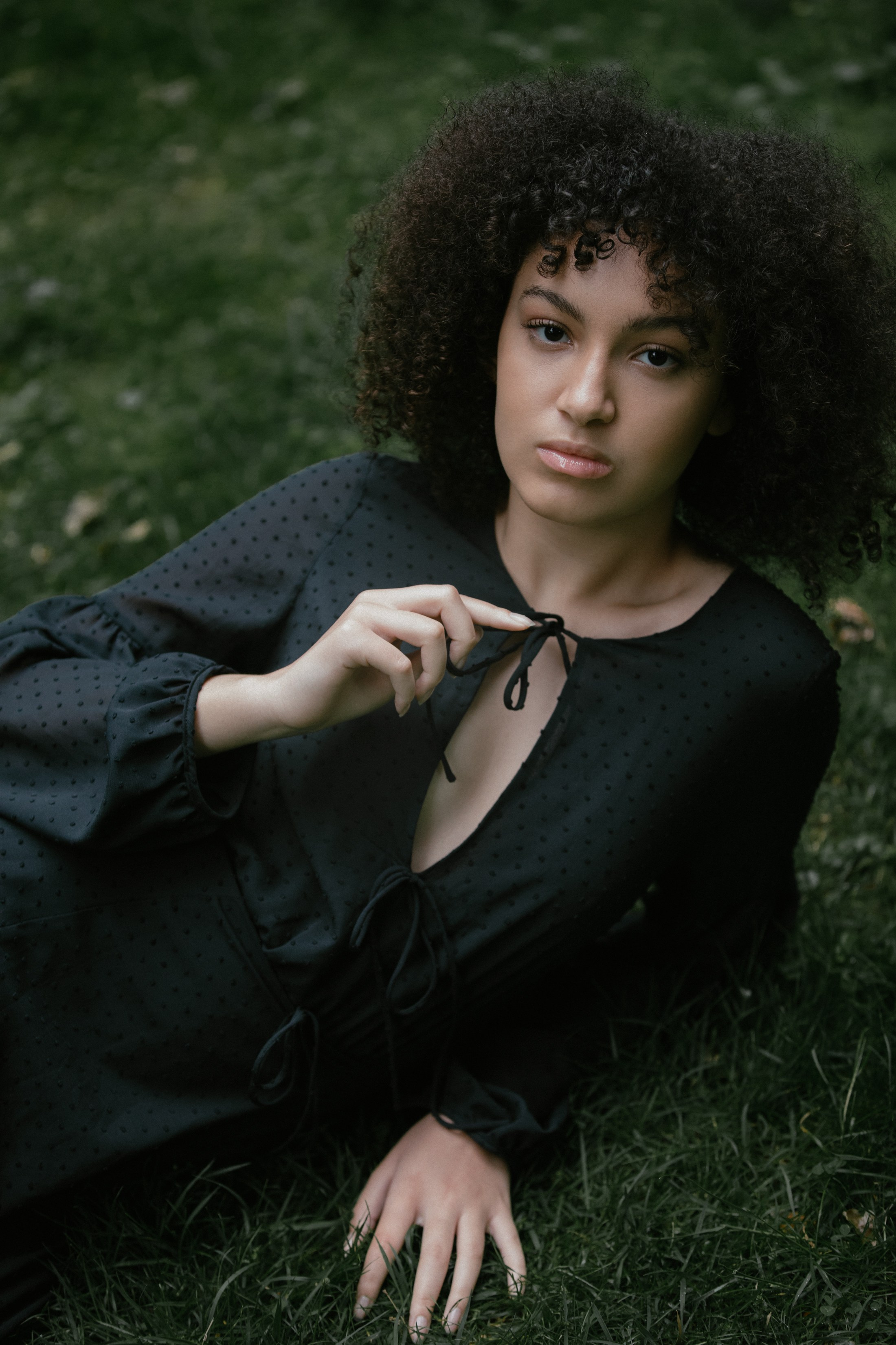 Woman holding dress tie, lying in grass, calm direct gaze