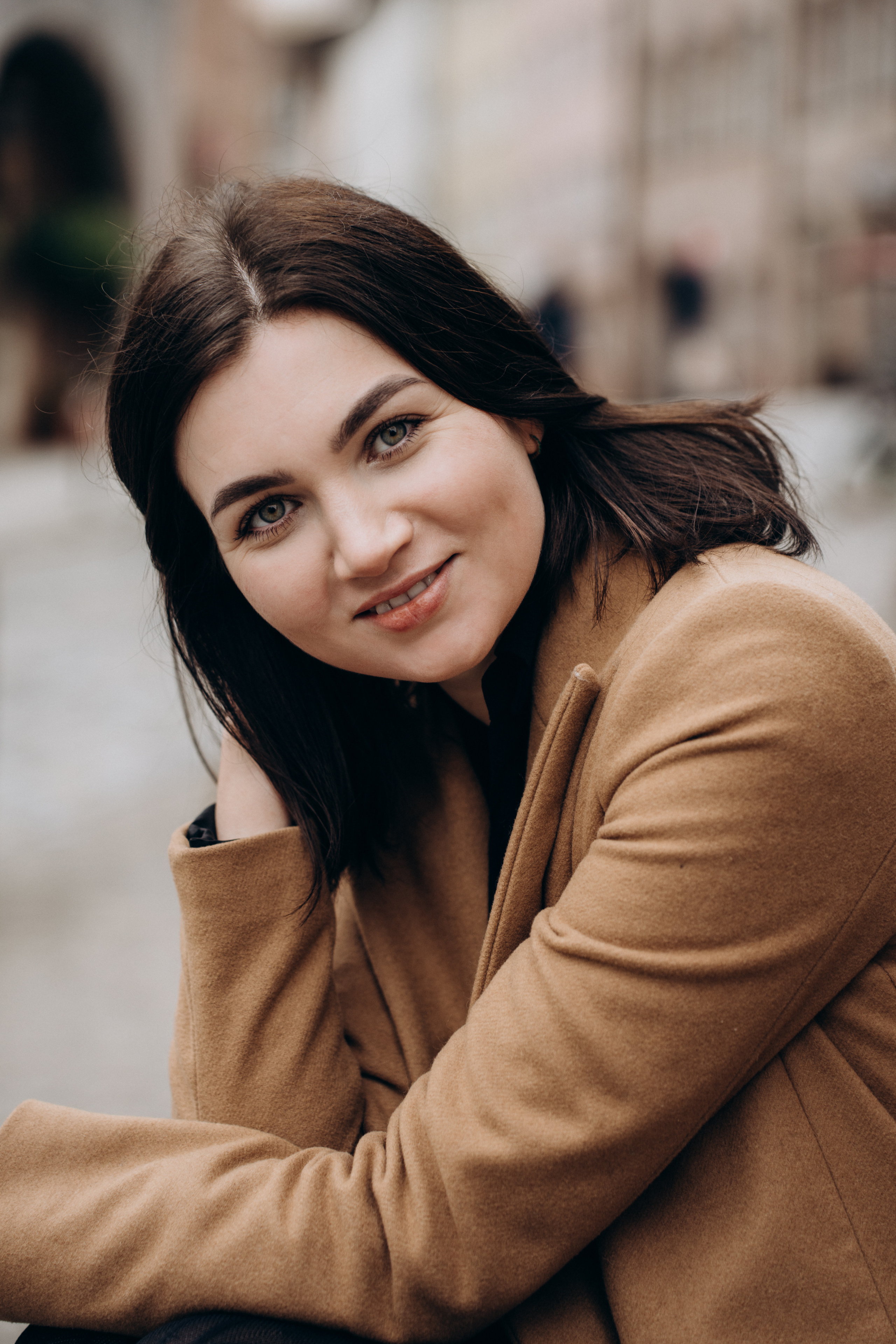 Porträt einer jungen Frau mit dunklem Haar und beigem Mantel – natürliche Einzelfotografie in urbaner Umgebung, aufgenommen von Natalja Glischev