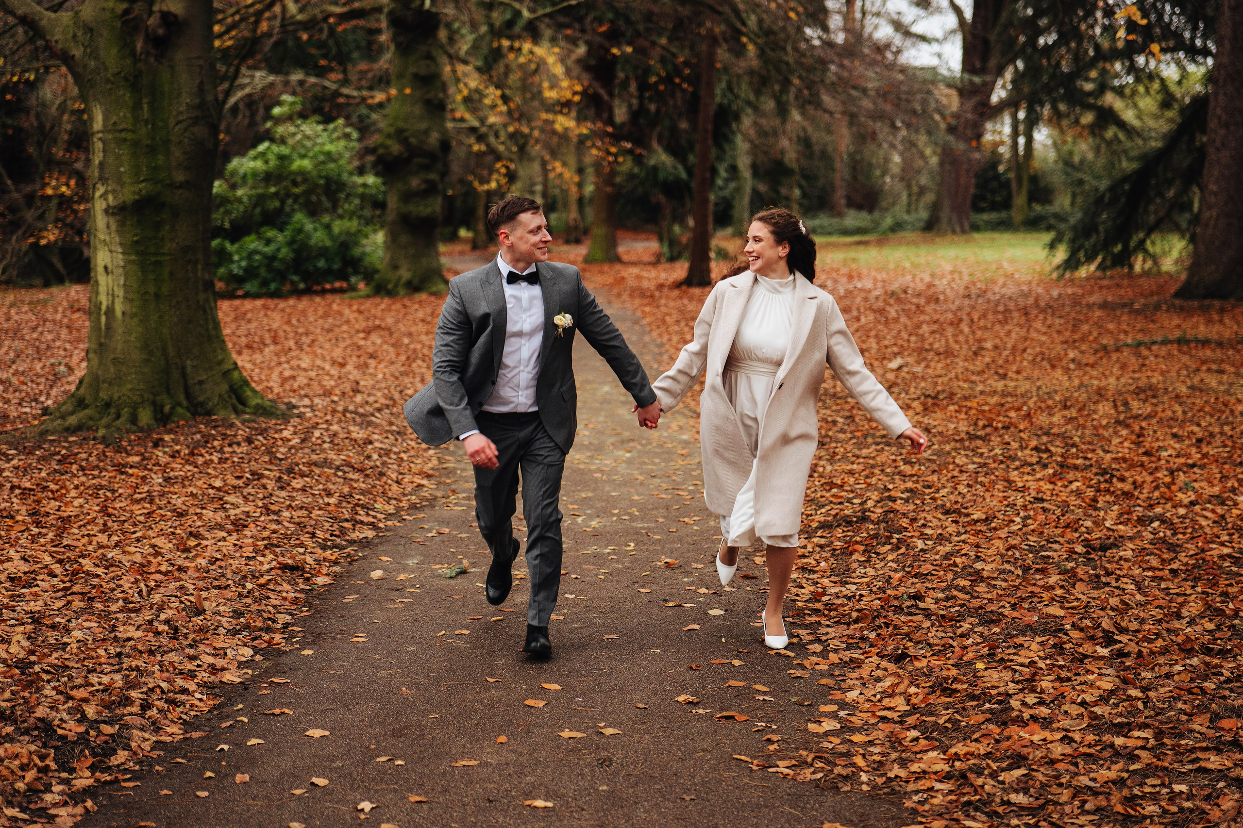 bride and groom running while holding hands in autumn park
