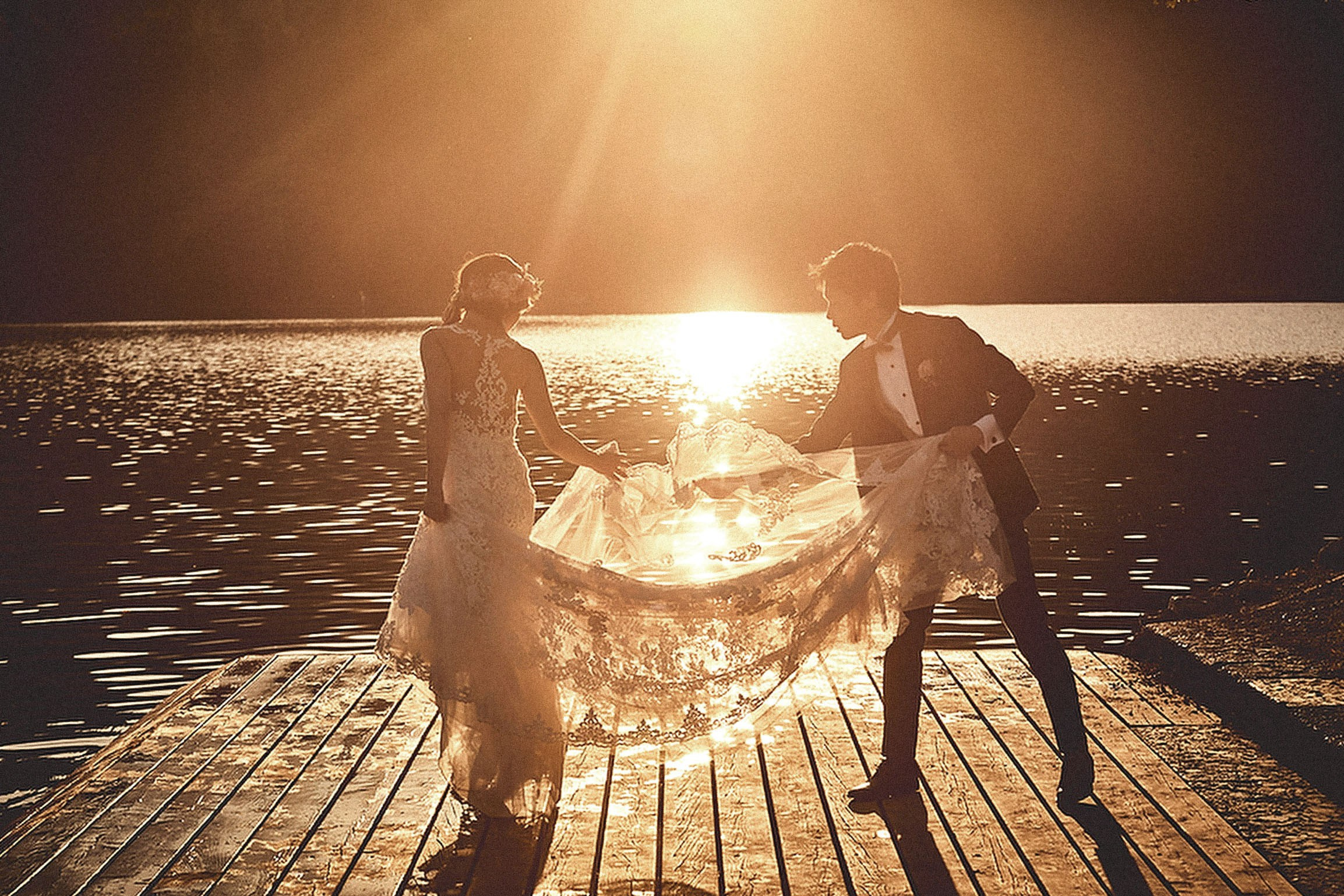 As the late afternoon sunlight illuminates them from behind, a groom is seen adjusting his bride's veil in the golden sunlight.