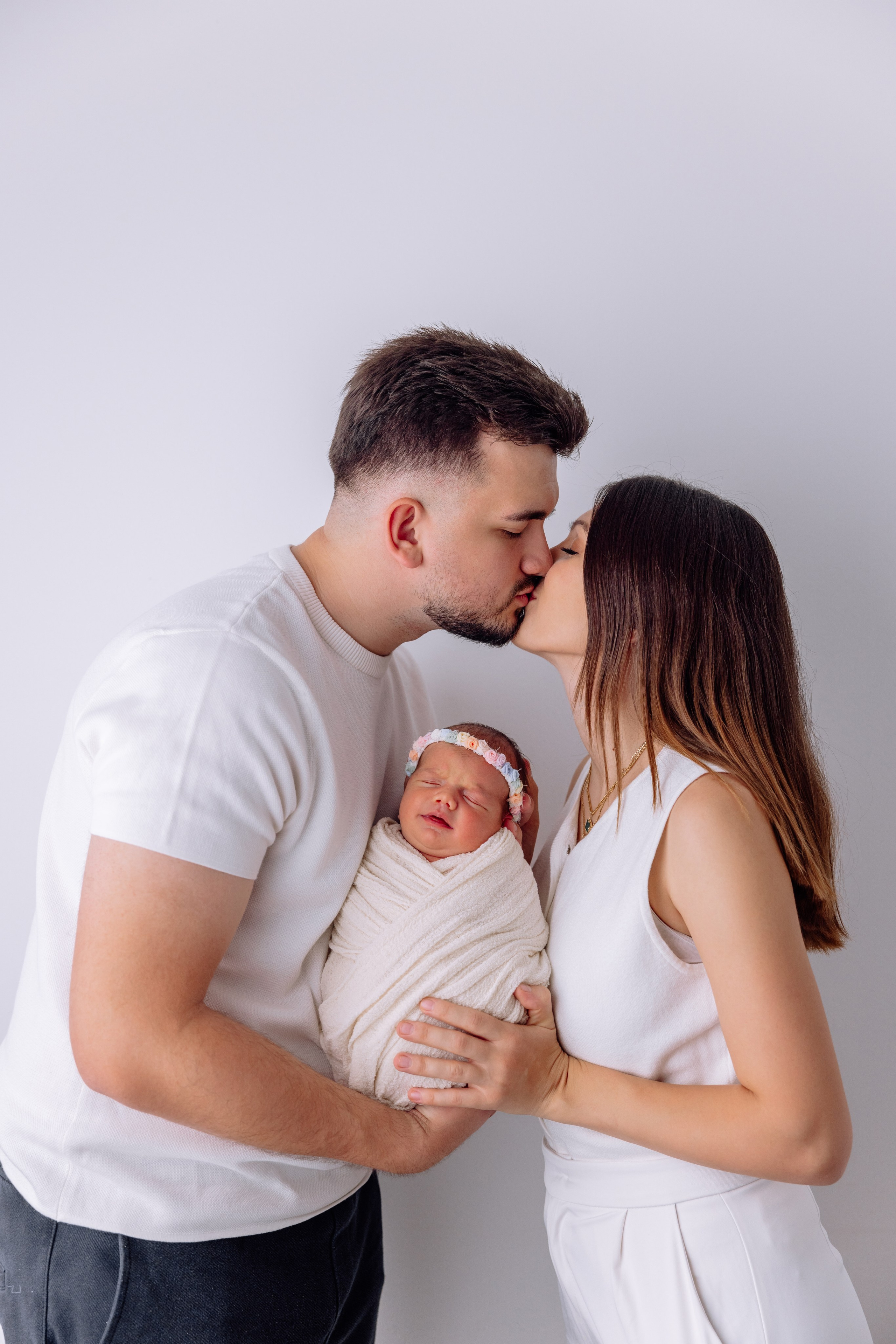 Familienfotoshooting zuhause in München – Mama und Papa küssen ihr Neugeborenes zärtlich auf die Wangen