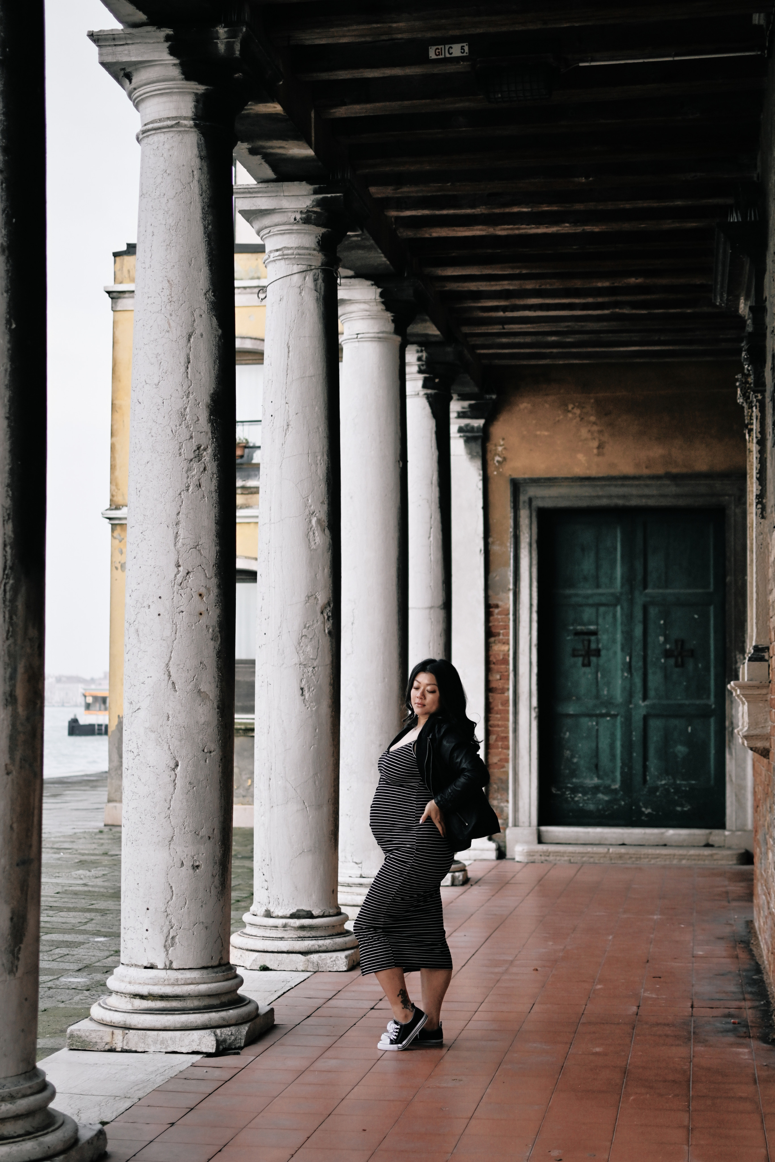 Against a backdrop of crumbling brick walls and ivy-covered archways, a pregnant woman stands in a Venetian alleyway, her flowing dress and loose hair caught in a gentle breeze. The city's timeless beauty echoes the anticipation of new life.