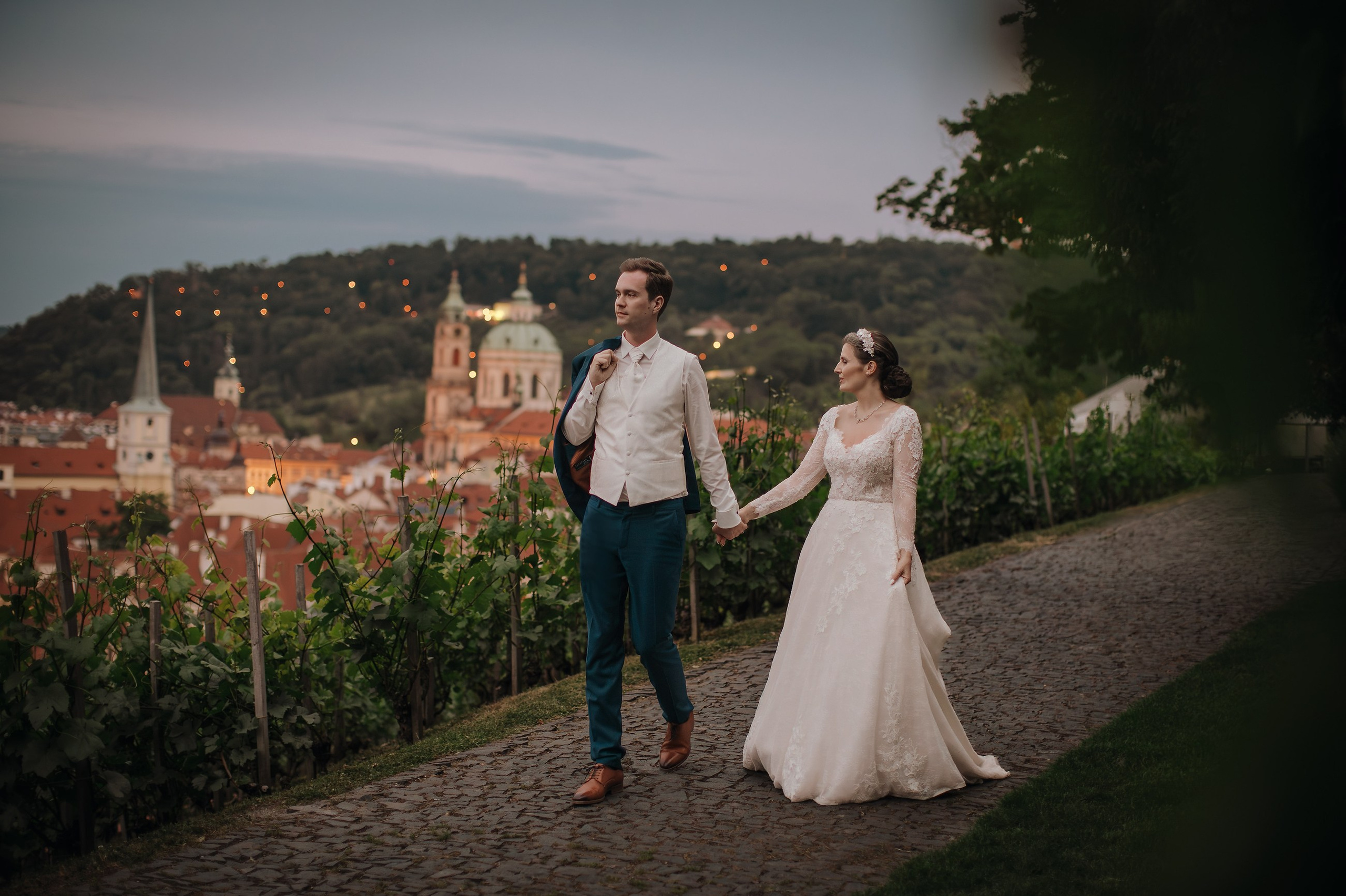 Newlyweds stroll through the historic vineyards of the Villa Richter under Prague Castle at dusk during their Prague wedding celebrations.  