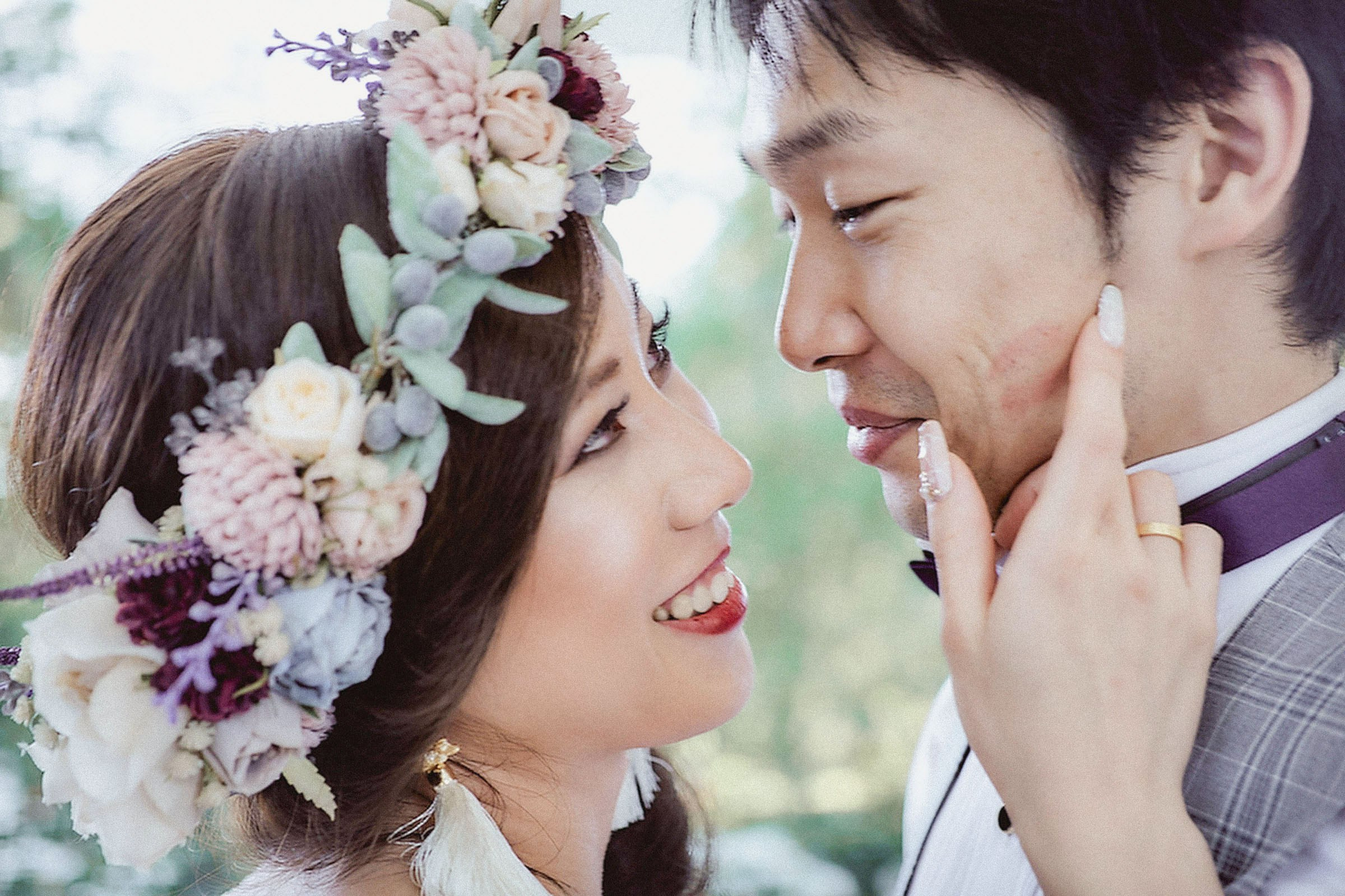 A Japanese bride, wearing a floral headpiece lovingly strokes the face of her groom as they stare into each other's eyes.