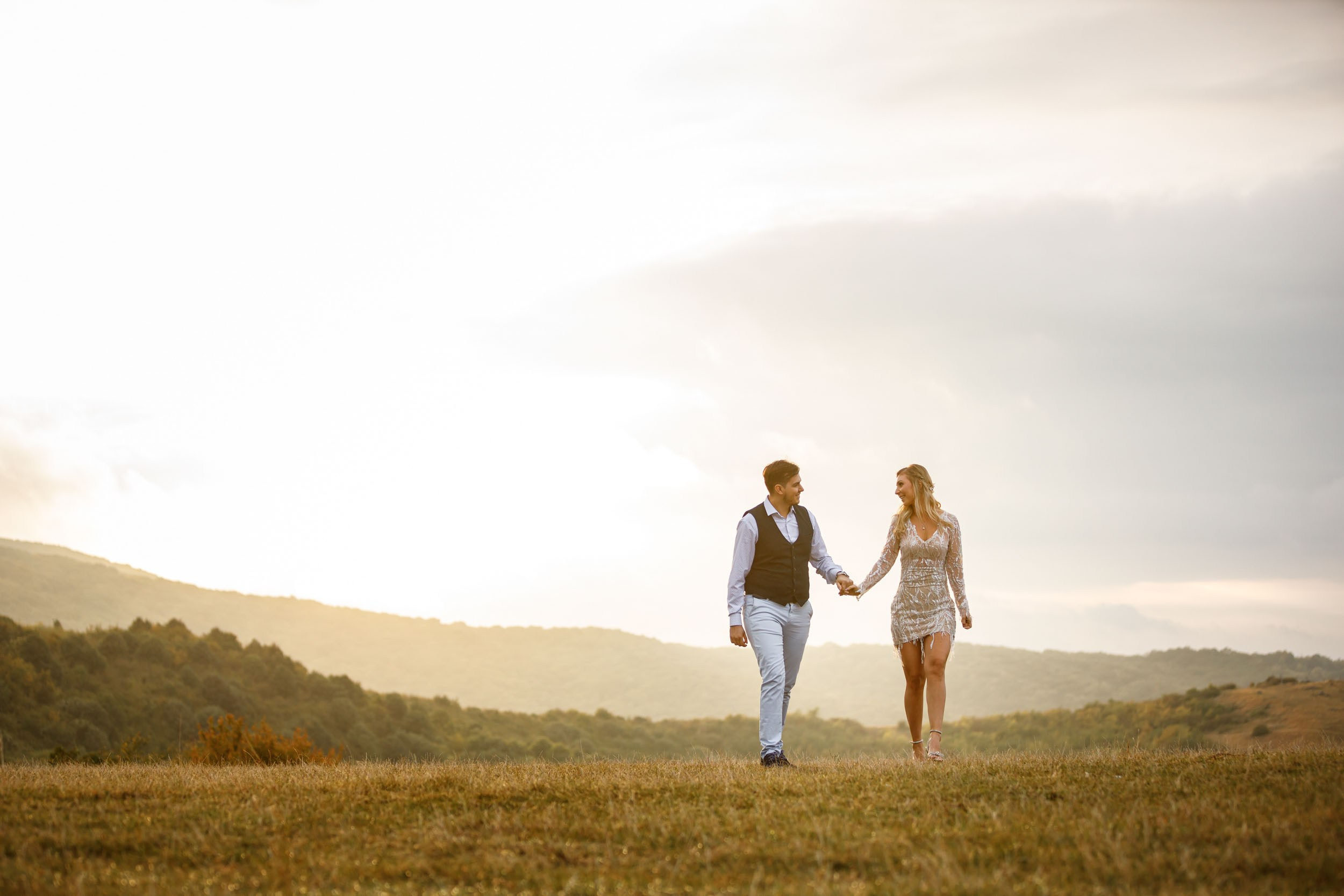 Topli tonovi zalaska jesenjeg sunca obasjavaju mladence u šetnji kroz prostranu livadu