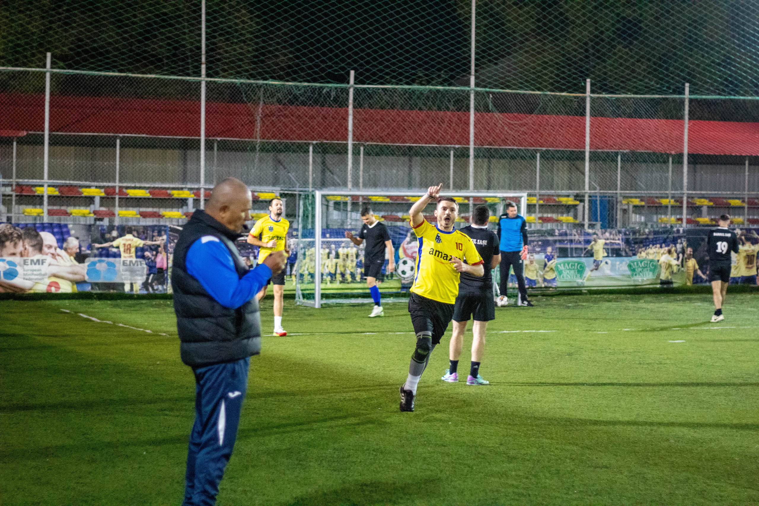 Football player in yellow shirt pointing and celebrating a goal during a nighttime match.
