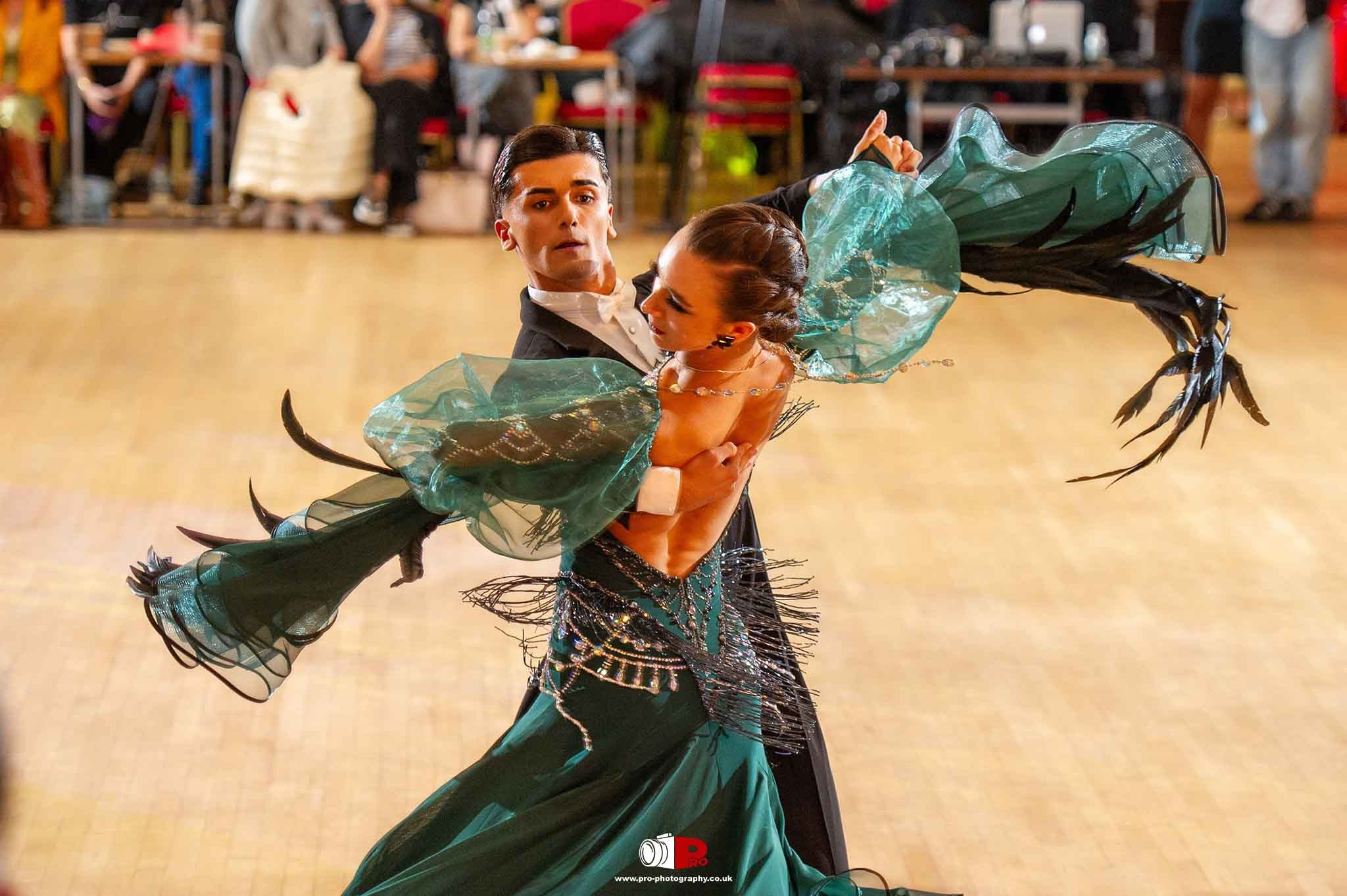 A dance couple performing in a striking green ballroom gown with flowing sleeves captivates the audience.