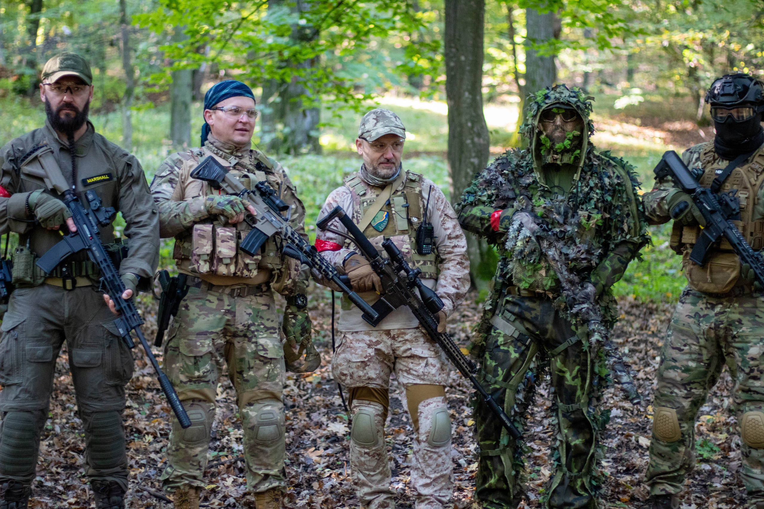 Airsoft team pointing rifles in formation while advancing through a forest area.