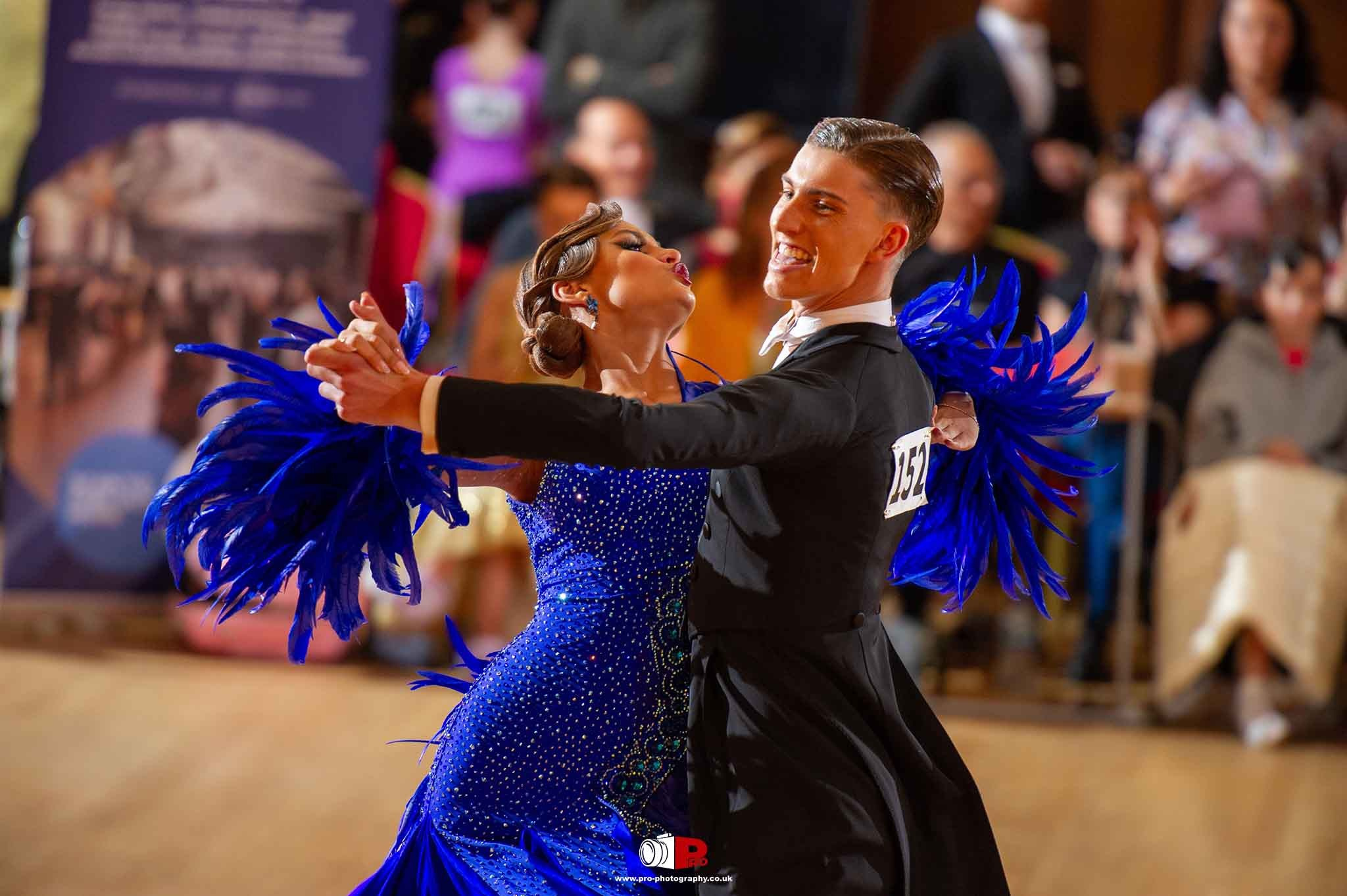 A poised ballroom dance couple in dazzling blue attire performing elegantly during a dance championship, mesmerizing the audience.