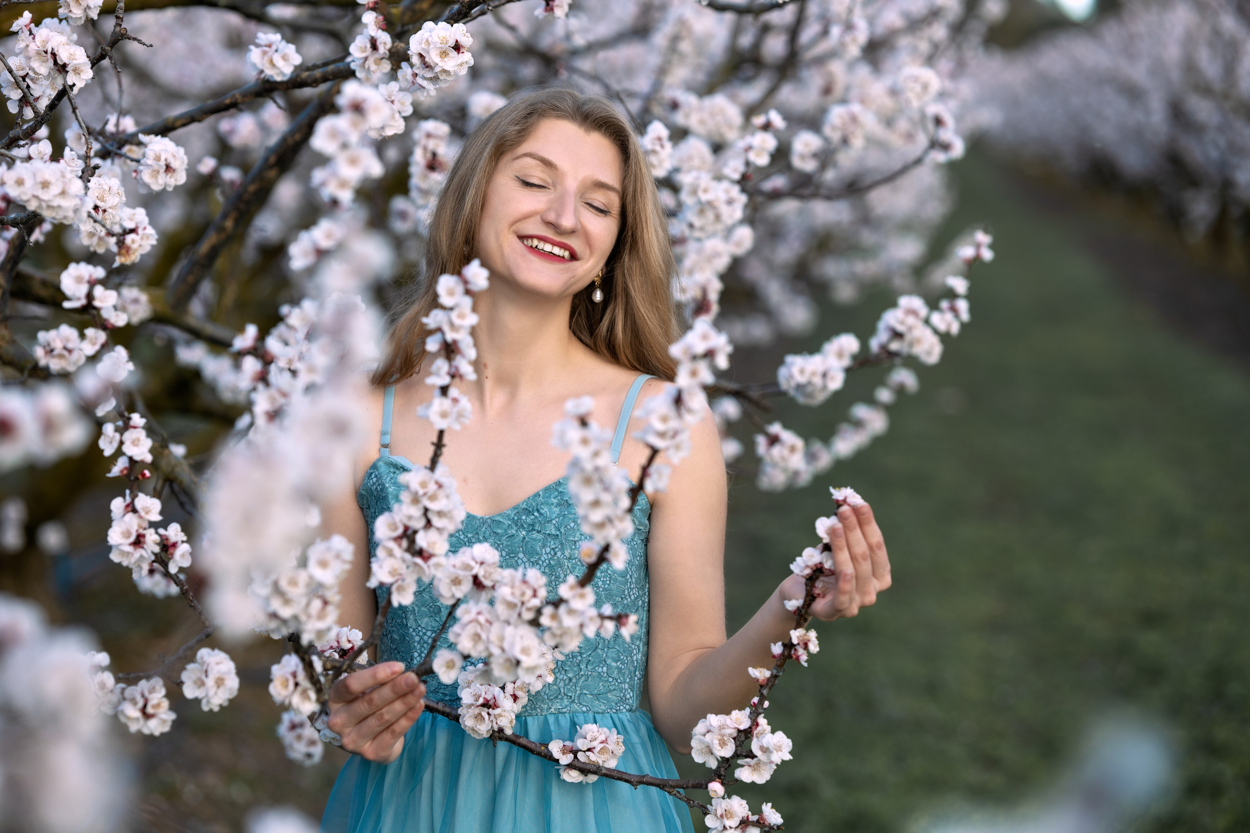 Gros plan sur une jeune femme blonde habillée en belle robe dans un verger en fleurs dans le sud de la France.