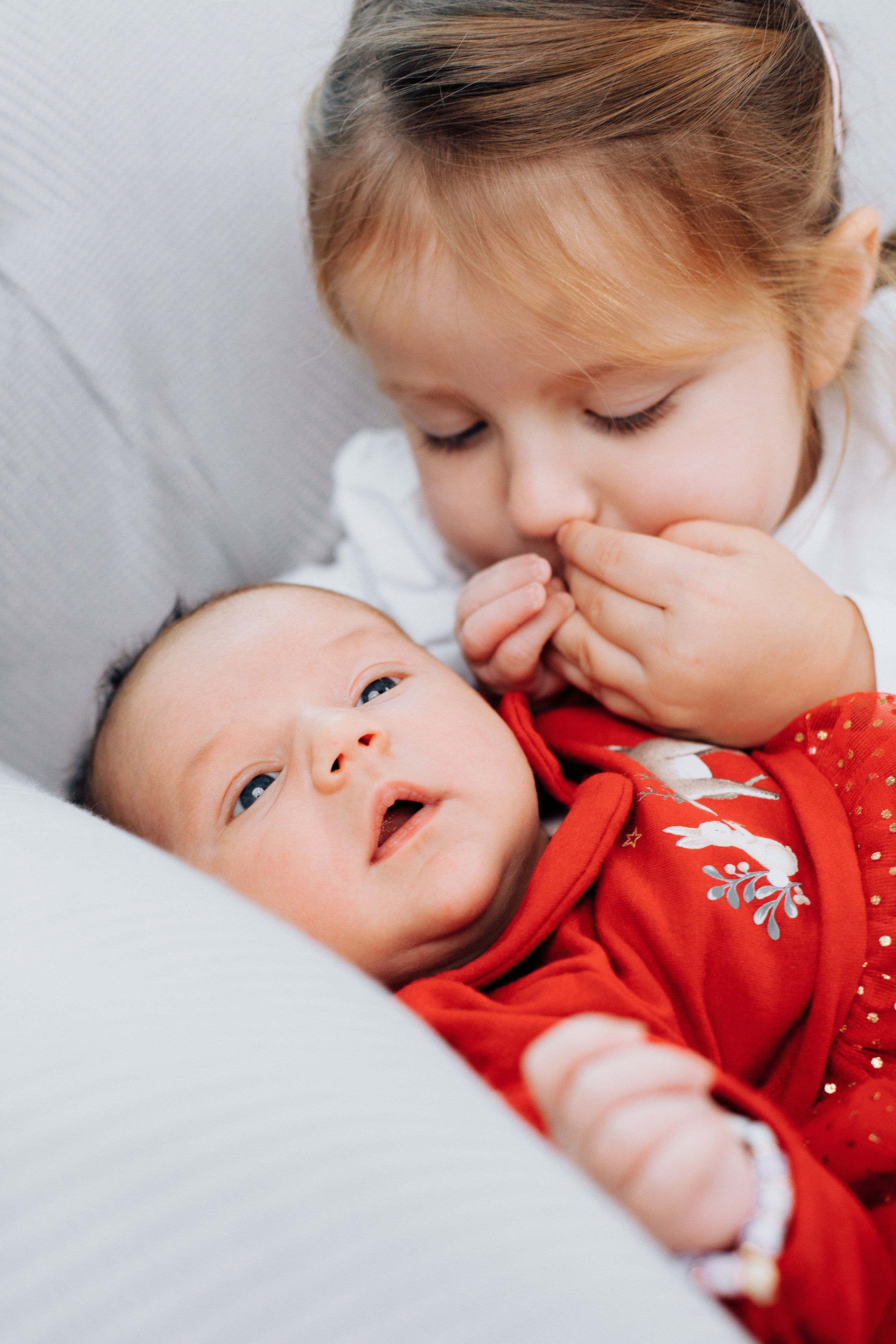 Die große Schwester küsst liebevoll die kleine Babyhand. Ein süßer und liebevoller Geschwistermoment.