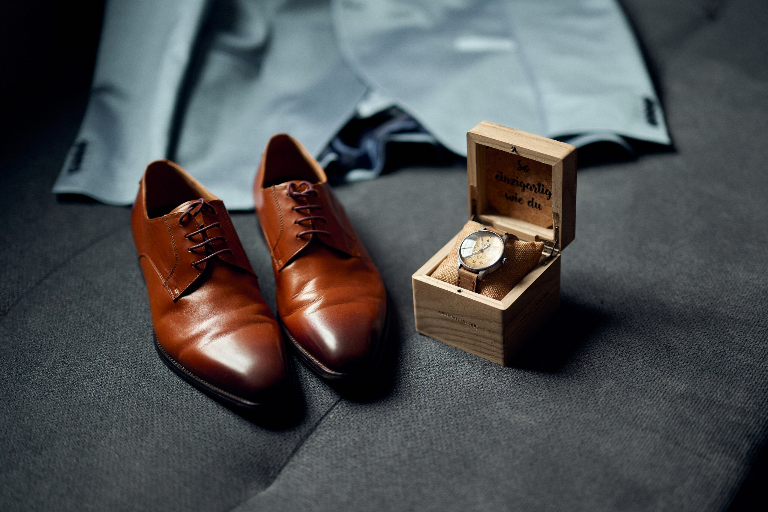 Detailaufnahme der Hochzeitsaccessoires von Nils – elegante Lederschuhe, eine personalisierte Uhr und sein Anzug vor der kirchlichen Trauung mit Feier im Schloss Meßkirch.