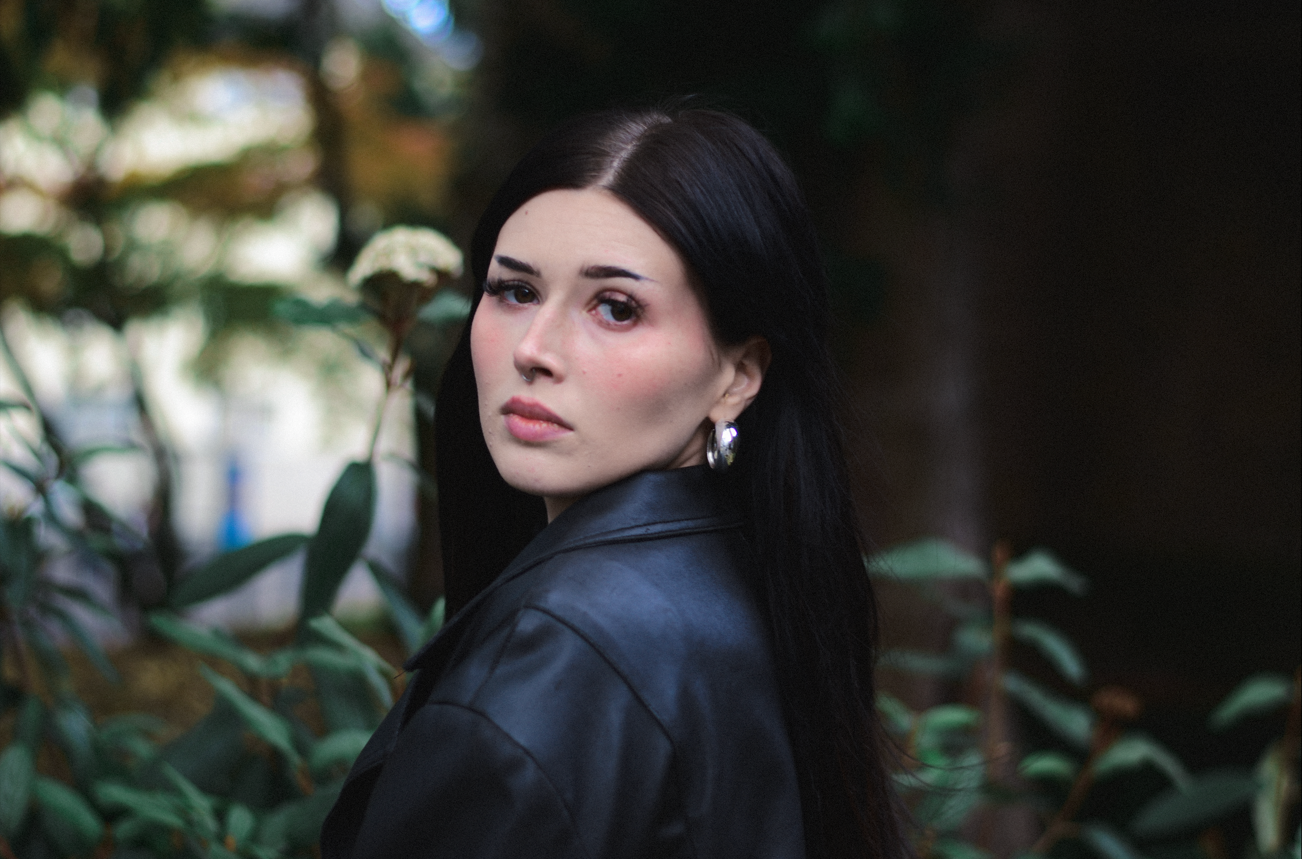 Porträt einer jungen Frau mit schwarzen Haaren und grünen Augen vor einem Naturhintergrund