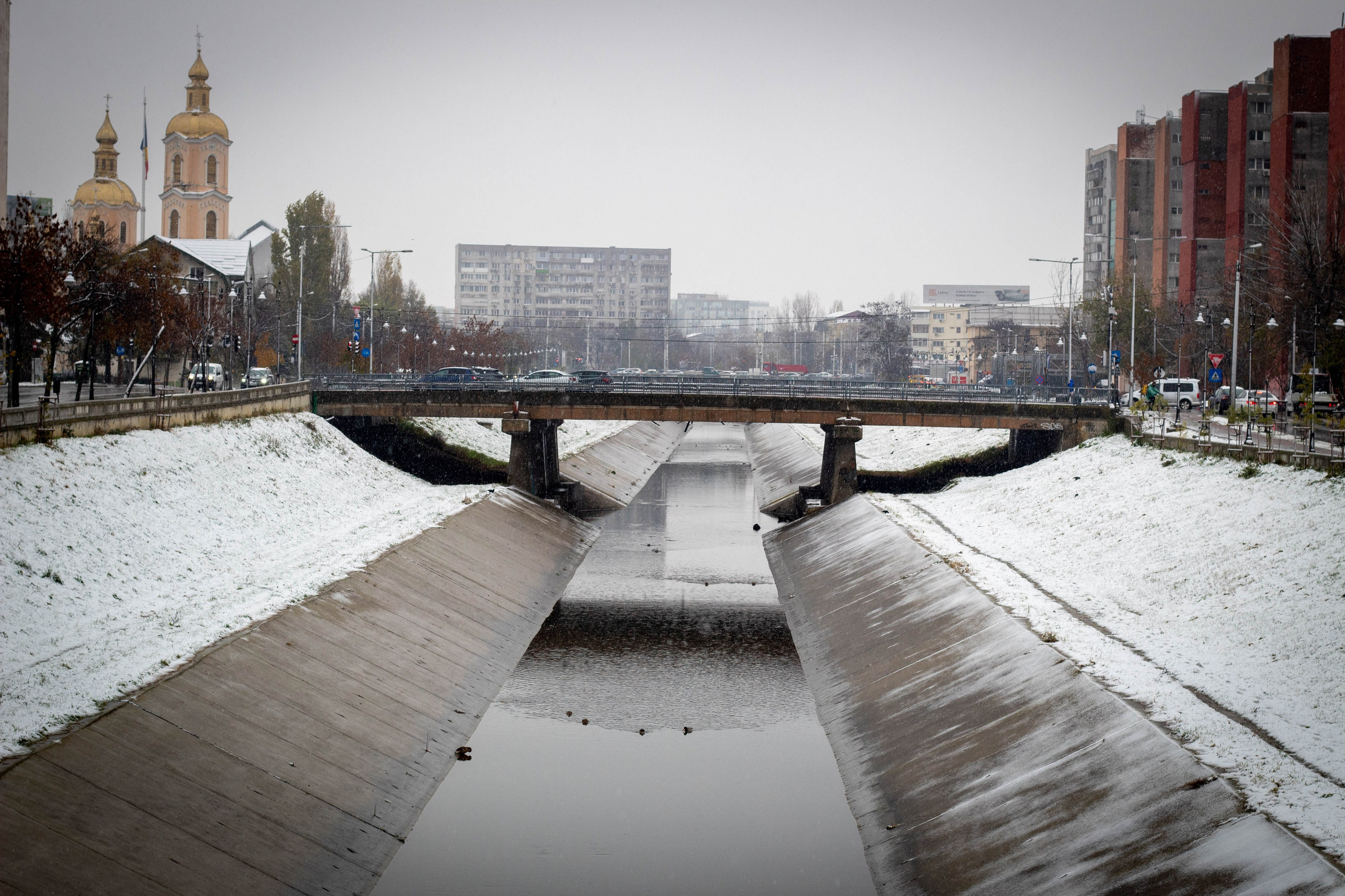 Snowy bridge and buildings in heavy fog, creating a moody winter cityscape.