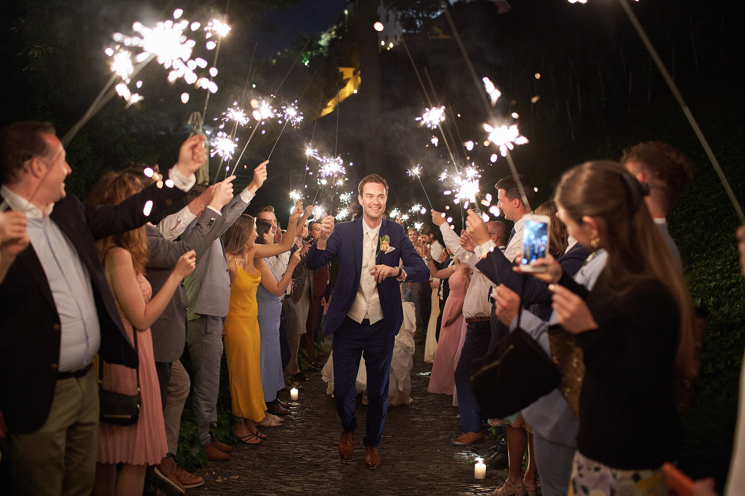 A  groom runs through a sparkler exit as his family & friends sing a popular song during wedding festivities at the Villa Richter in Prague.